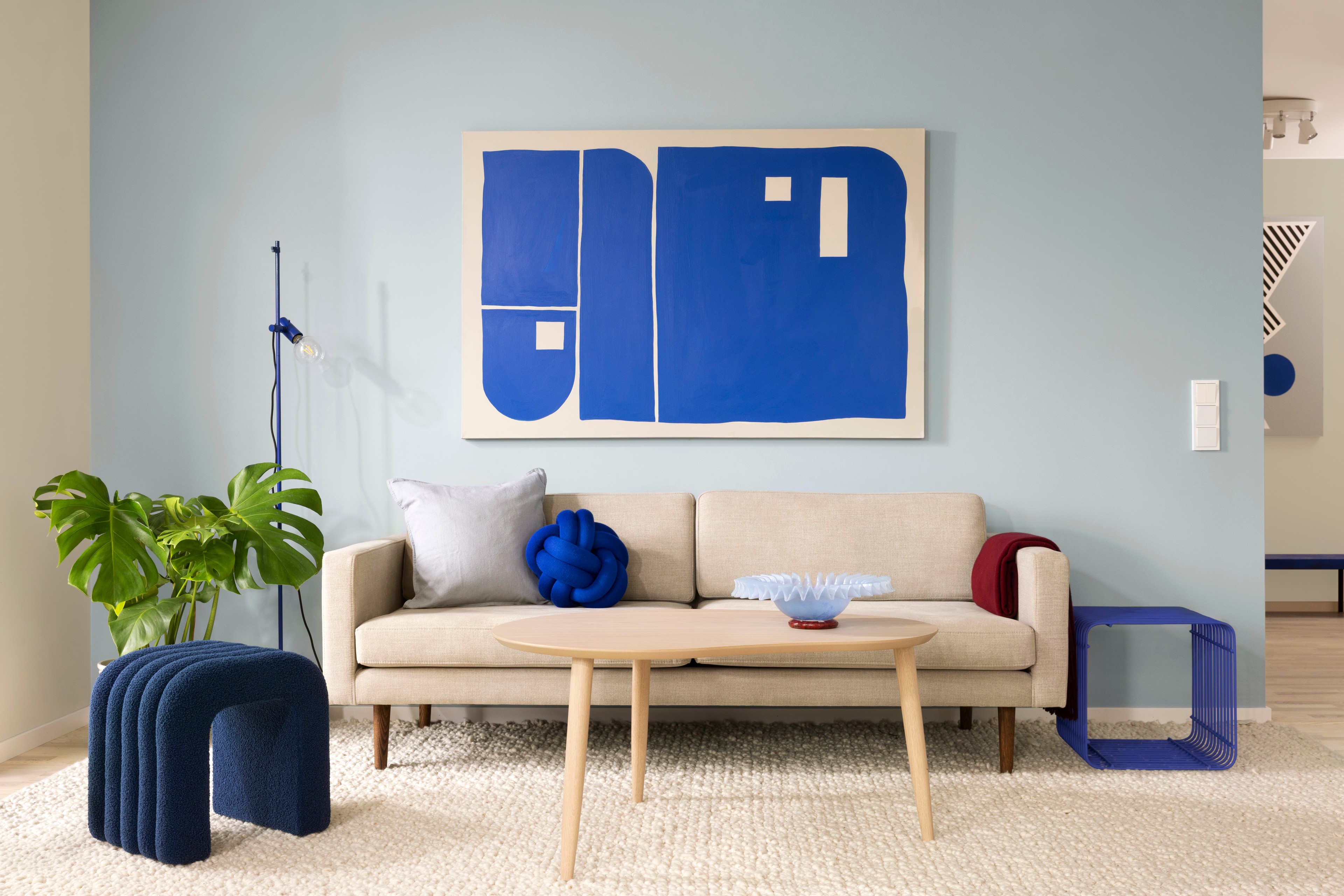 Modern vardagsrum med blå inslag och abstrakt konst Modern vardagsrum med beige soffa, abstrakt blå konstverk och stilfulla moderna inredningsdetaljer.