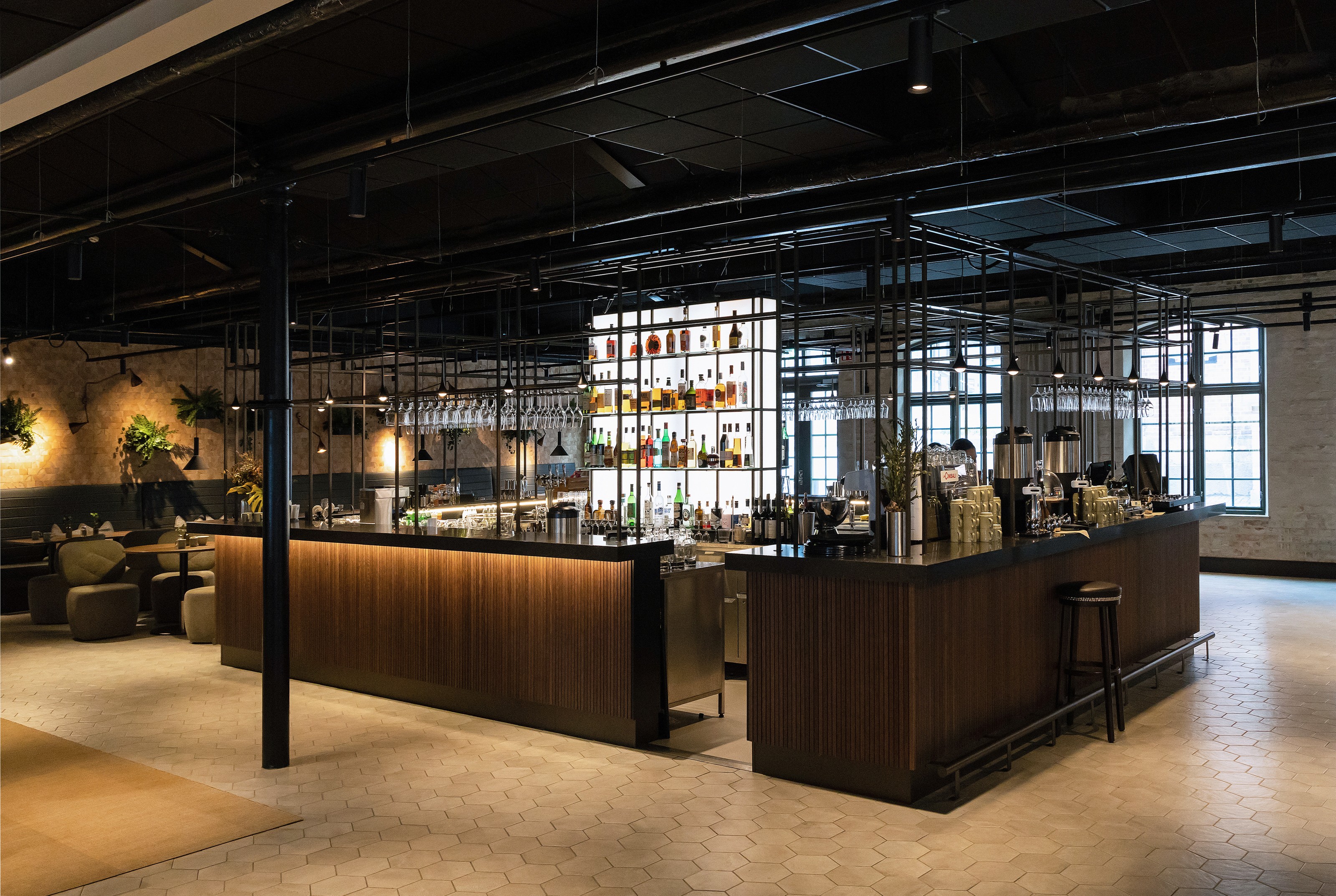 Modern bar med hexagonala golvplattor, trädiskar och en bakgrundsbelyst spritdisplay.
