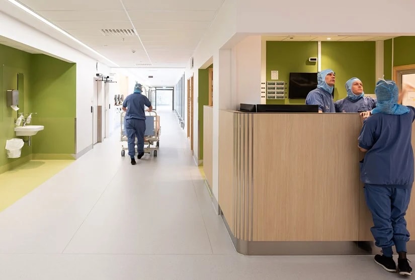Karolinska Hospital in Huddinge Hospital corridor with medical staff in scrubs, engaging at a reception desk and moving equipment.