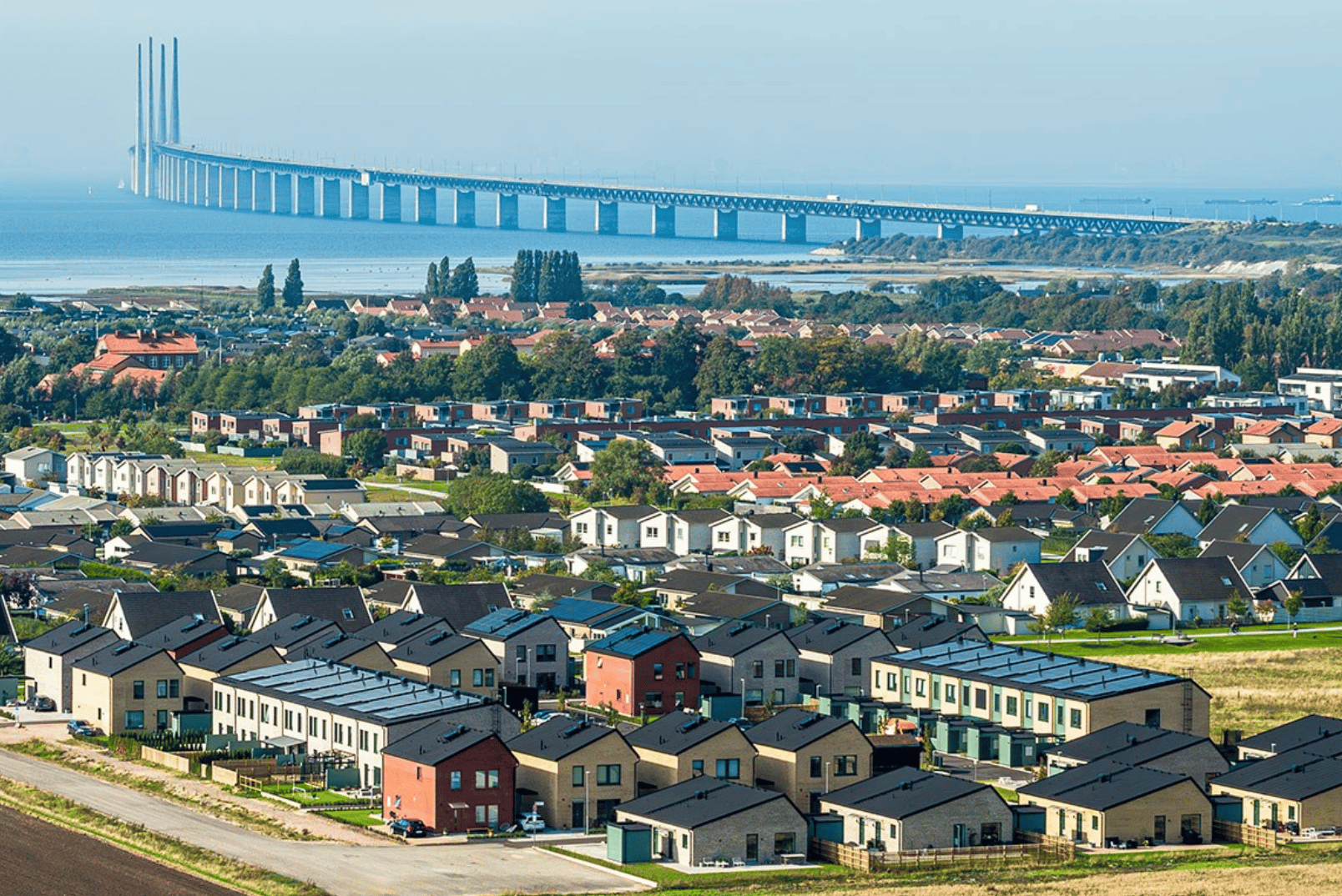 Flygbild av förortshus med Öresundsbron över havet i bakgrunden.