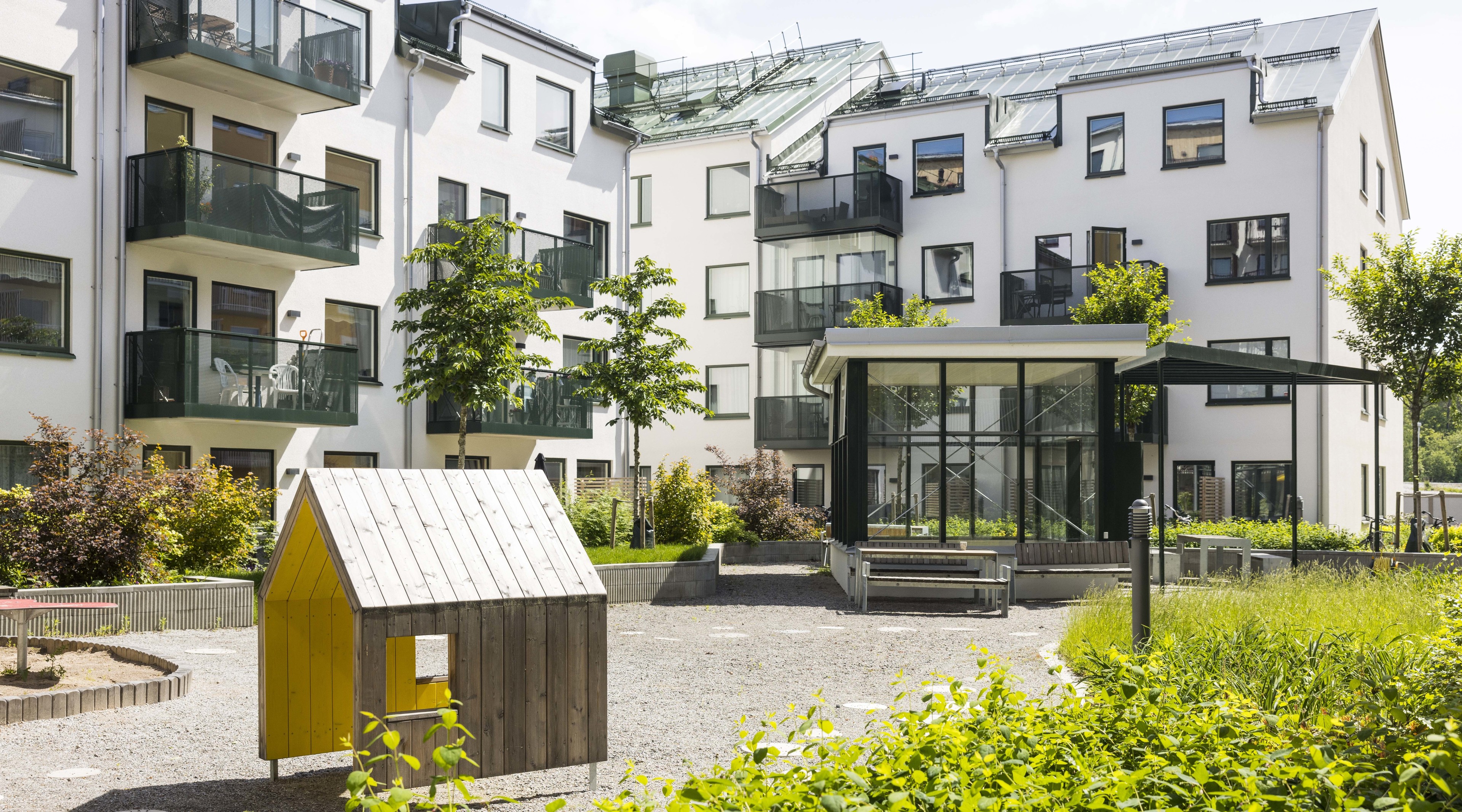 Moderna vita lägenhetsbyggnader med balkonger som omger ett litet stadsnära trädgårdsområde.