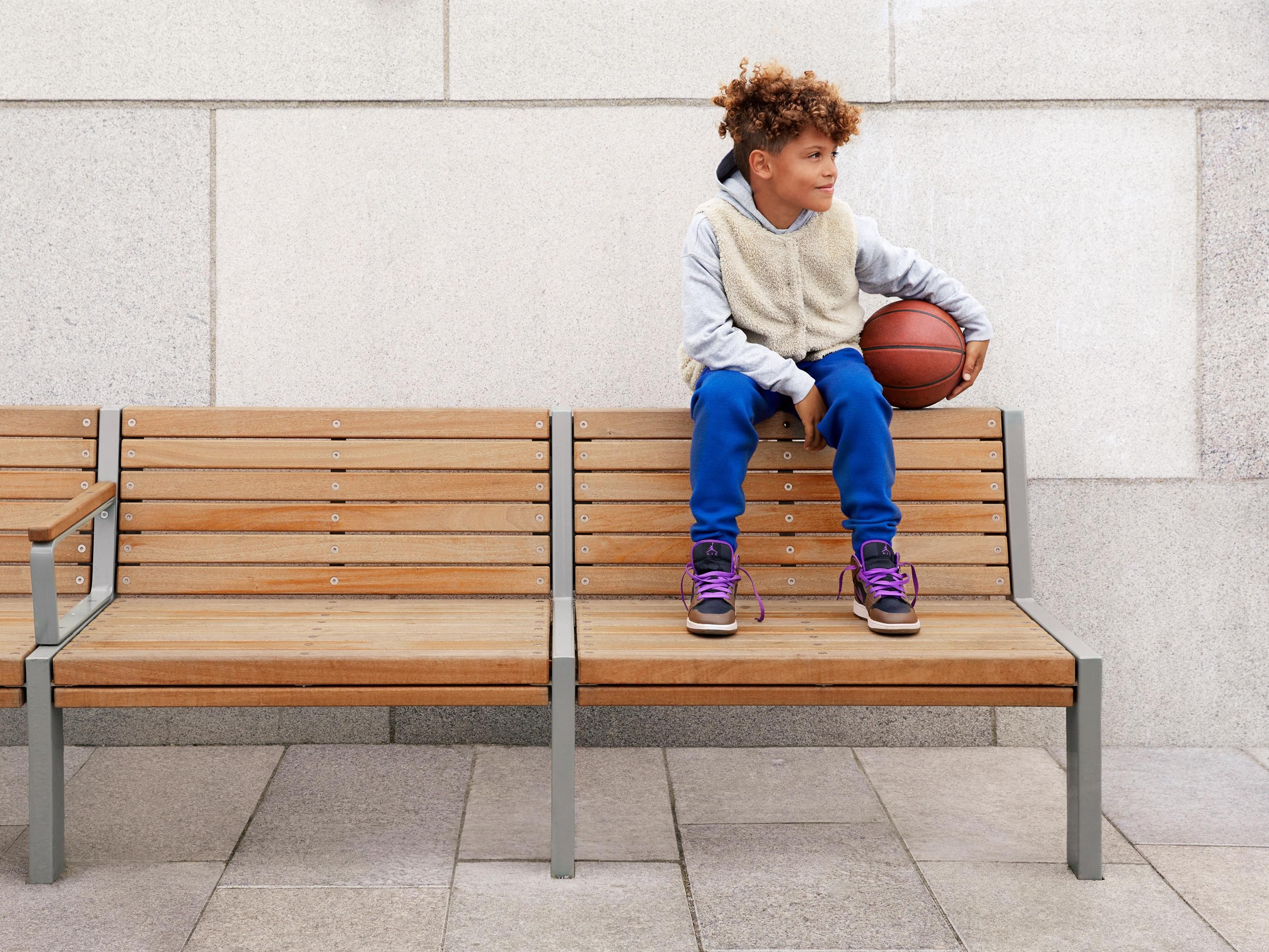 Pojke som sitter på ryggen av en bänk med en basketboll i handen