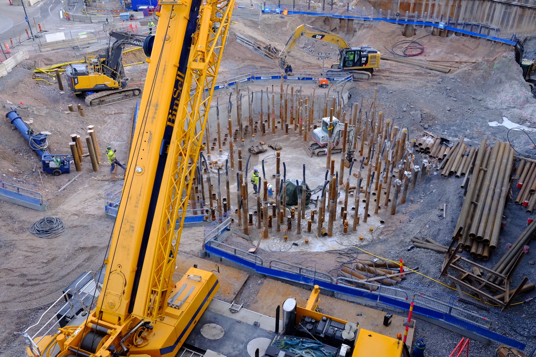 Construction site with heavy machinery and workers installing a circular arrangement of piles.