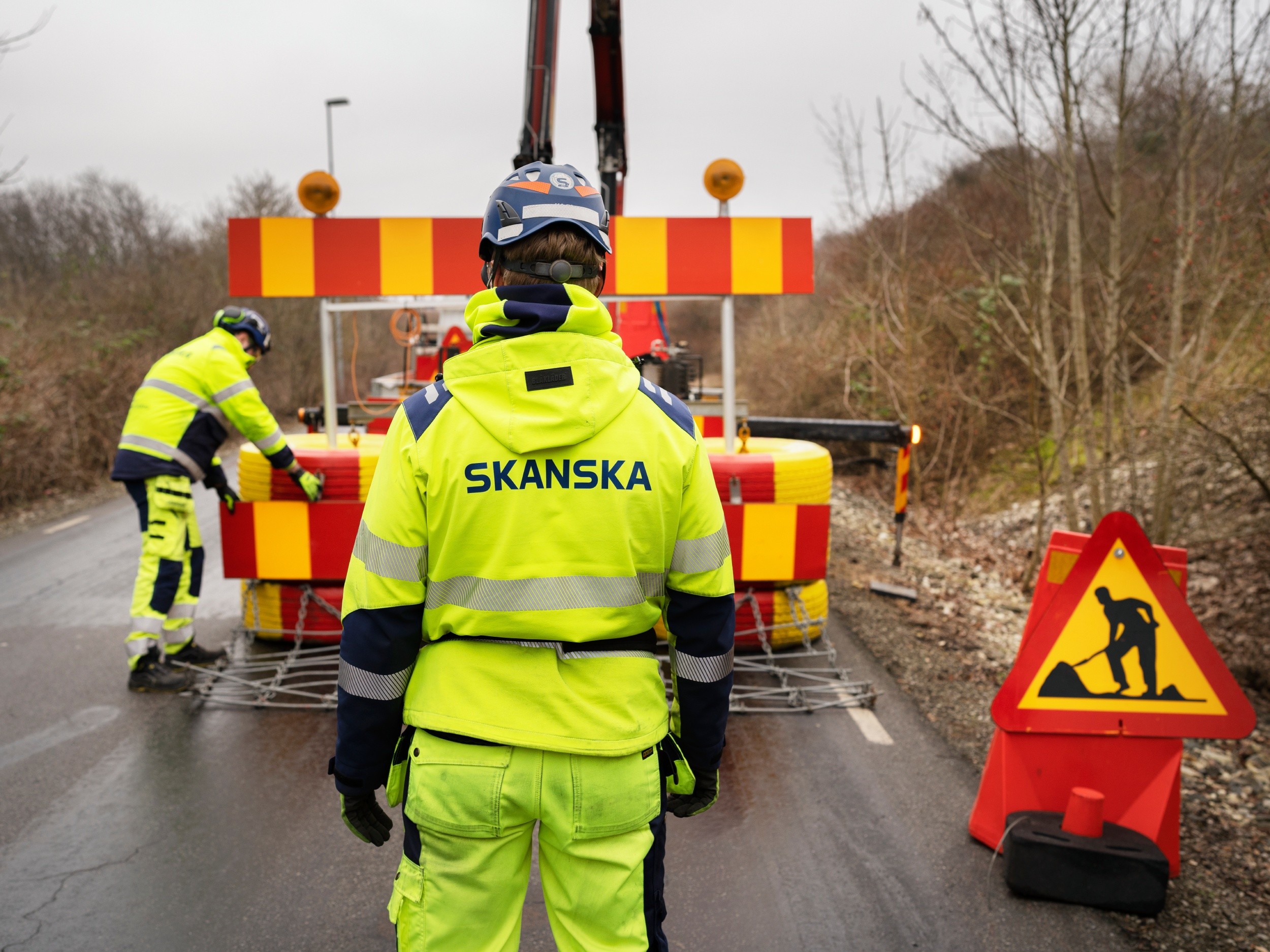 Byggarbetare i varselkläder sätter upp vägbarriärer med Skanska-märkning.