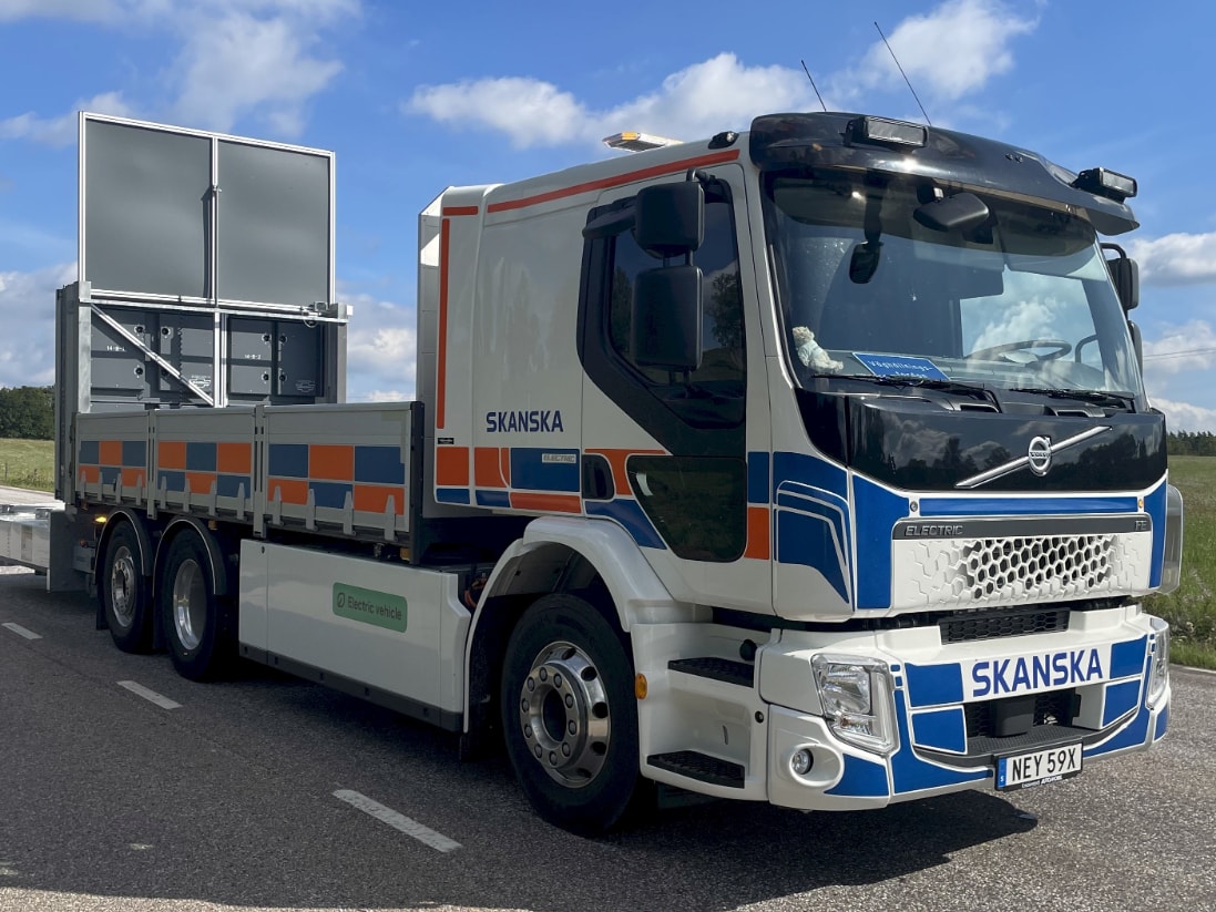 Electric Volvo truck with Skanska branding parked on a road under a blue sky.