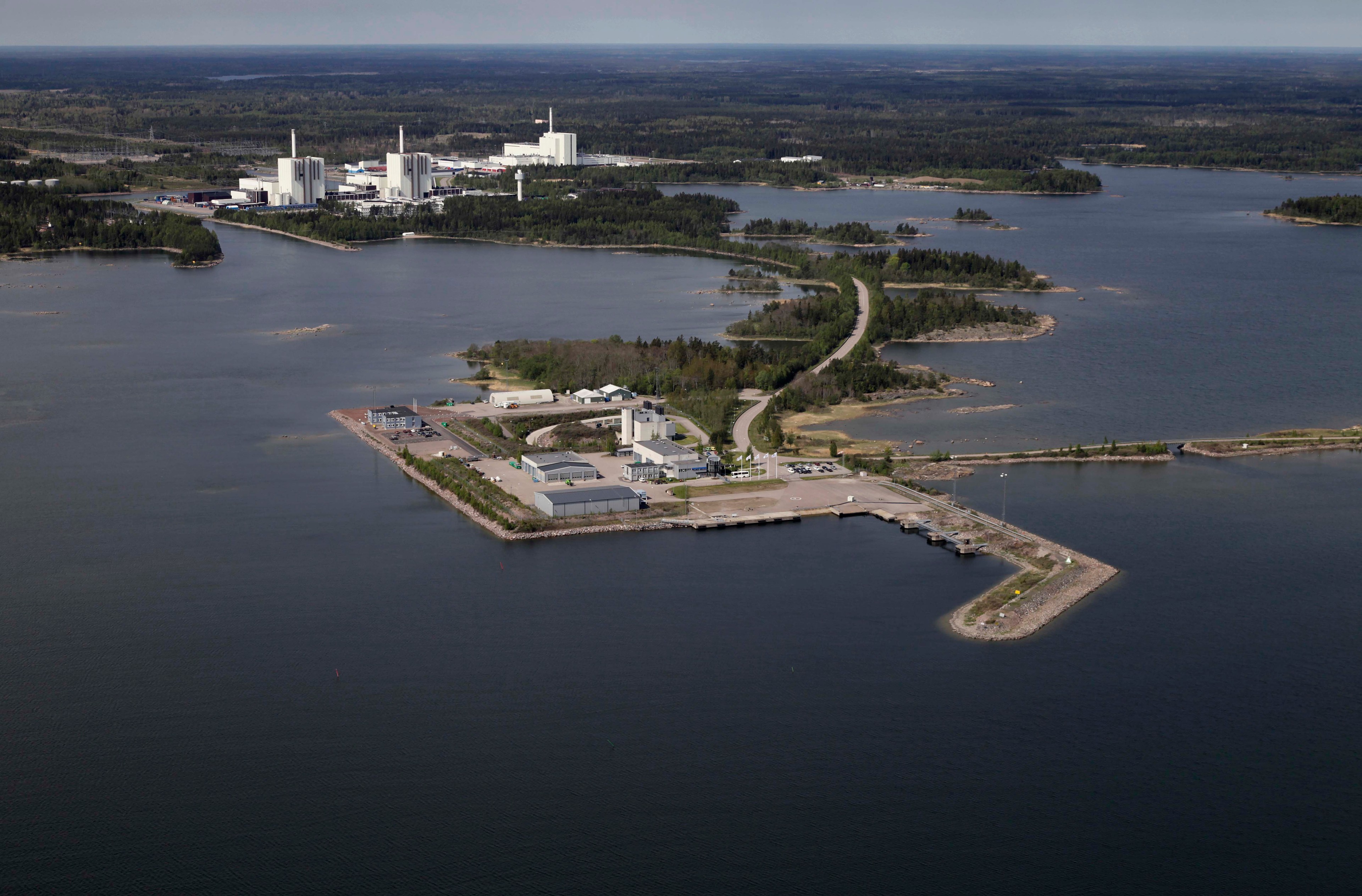 Kustnära industriell anläggning vid havet med klart blått vatten Flygvy över en kustnära industrianläggning med byggnader, vägar och omgivande vatten.