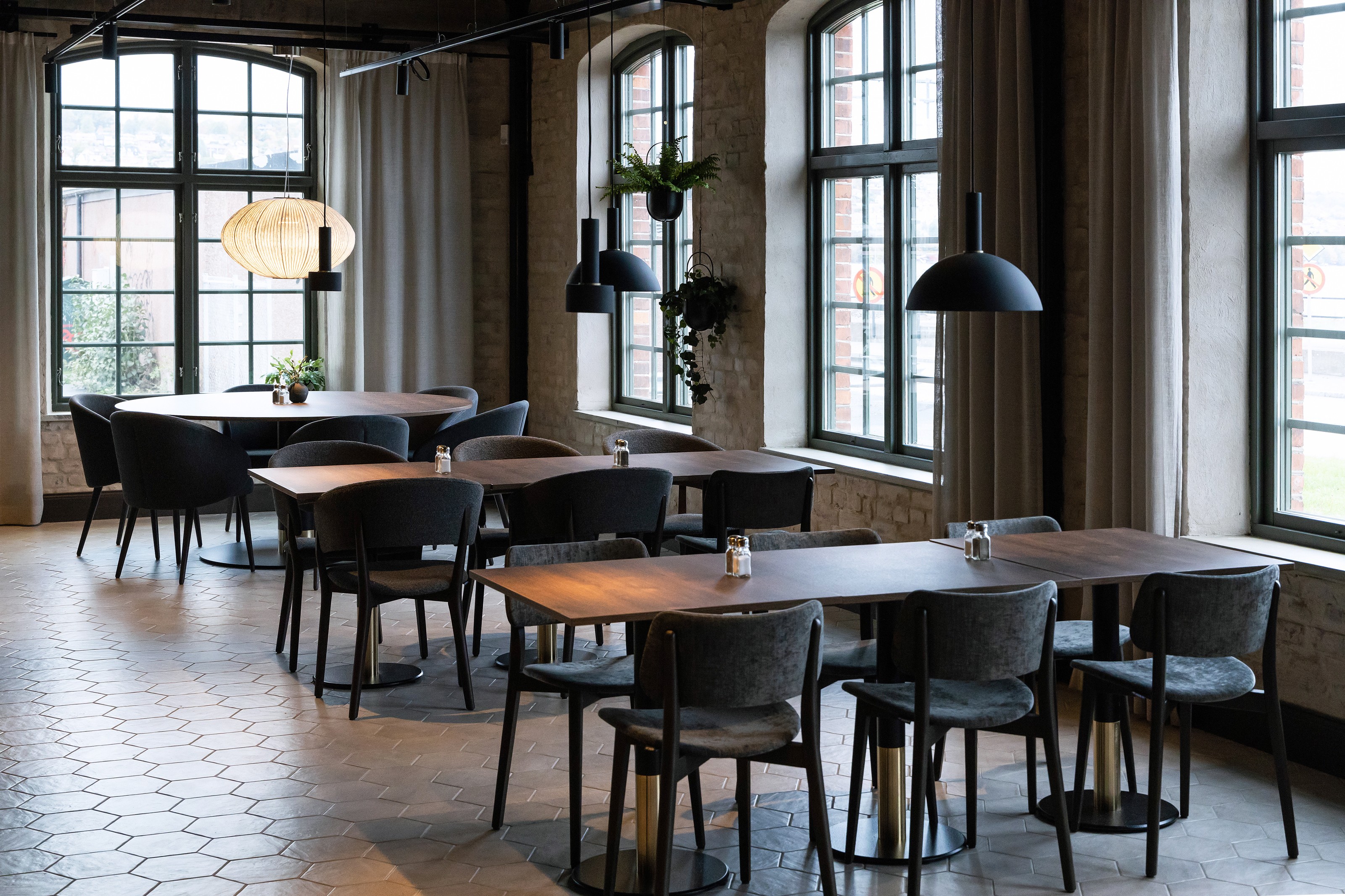 Modern caféinteriör med träbord, svarta stolar, stora fönster och hängande lampor.