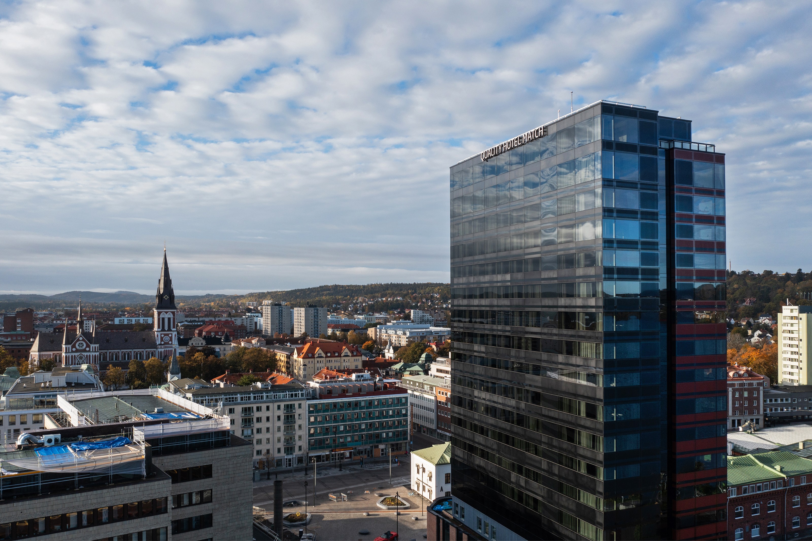 Modern glas kontorsbyggnad med stadsbild och molnig himmel i bakgrunden.