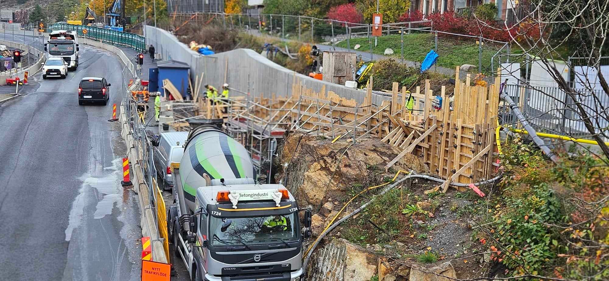 Byggarbetsplats med cementblandarbil och arbetare som bygger en betongvägg.
