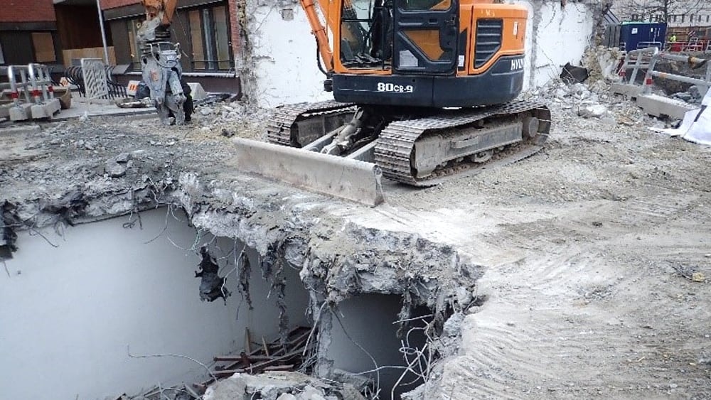 Maskin som håller på att riva ett betonggolv där man ser ner till våningen under.