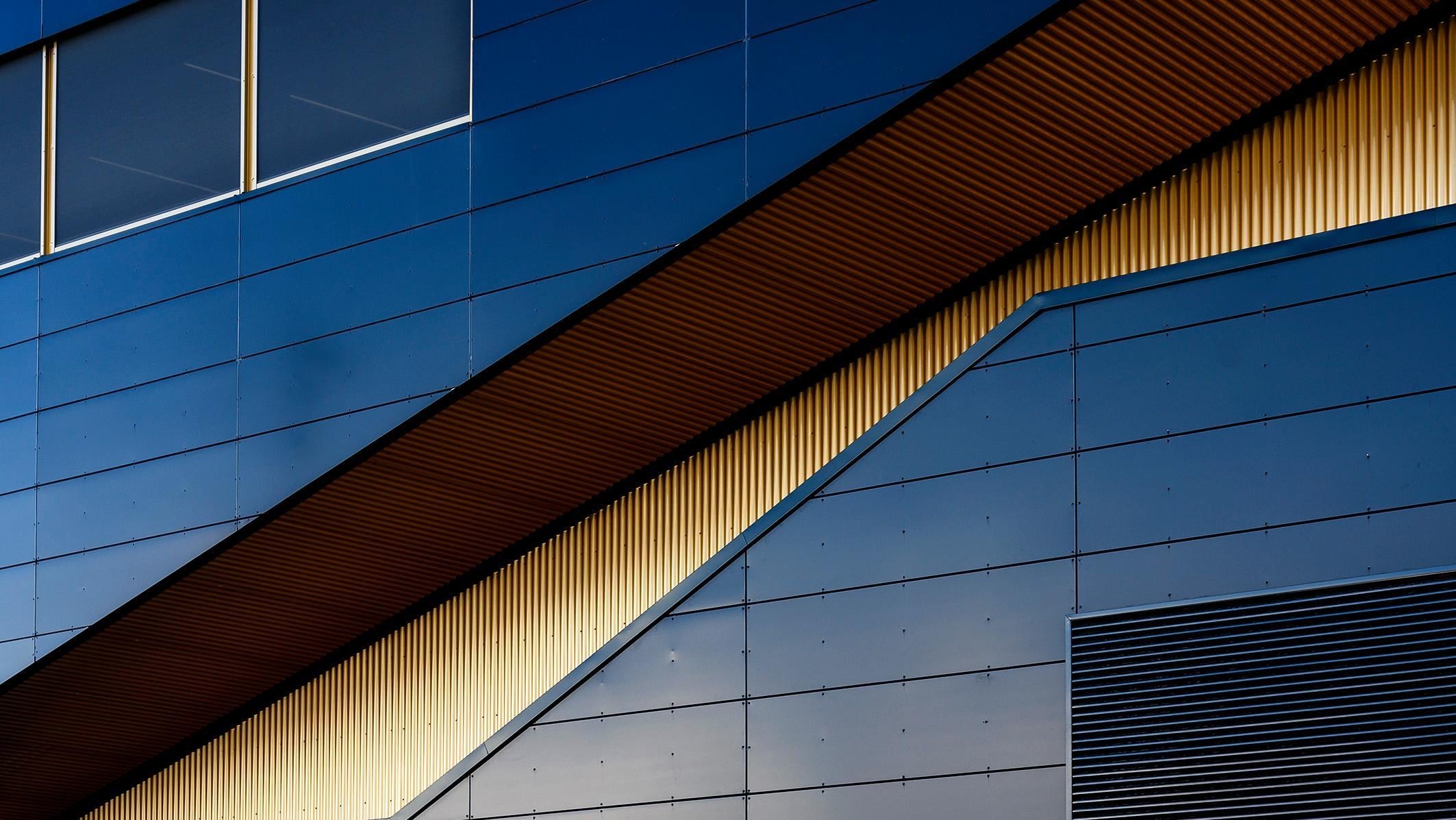 Modern byggnadsfasad med geometriska mönster, blå paneler och gyllene accenter.