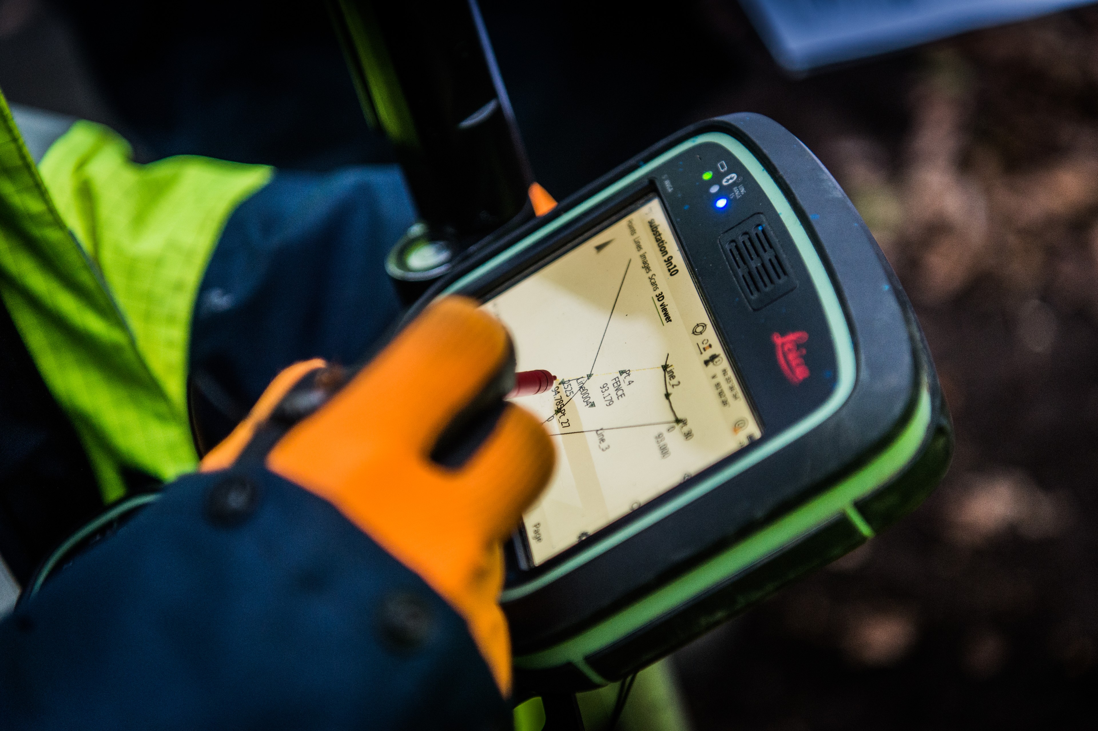 Measurement technicians use Leica GPS device for land mapping A gloved hand is handling a Leica GPS surveying device that displays a detailed map screen.
