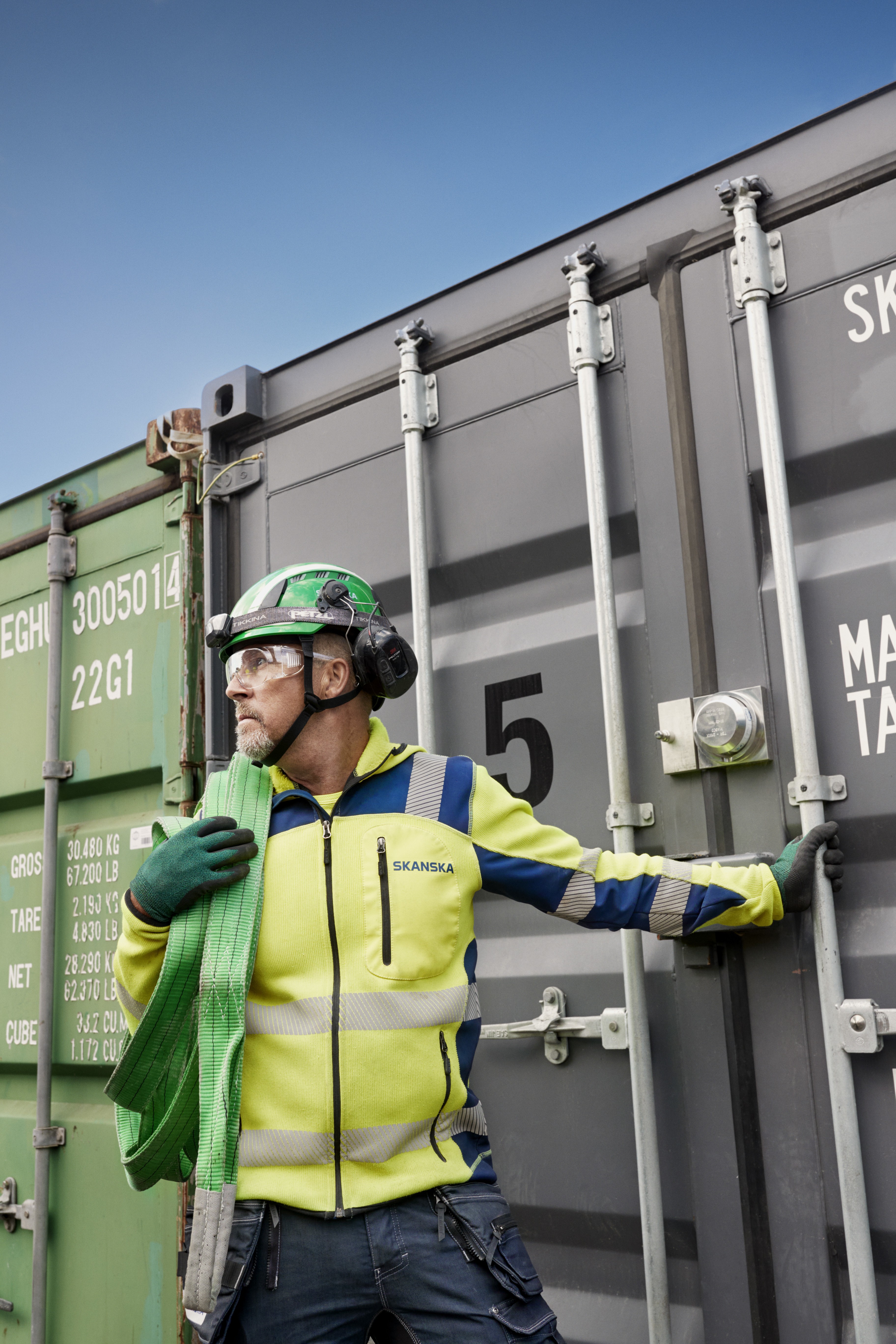 Construction workers handle shipping containers safely A construction worker in high-visibility clothing stands by a shipping container and holds a green strap.