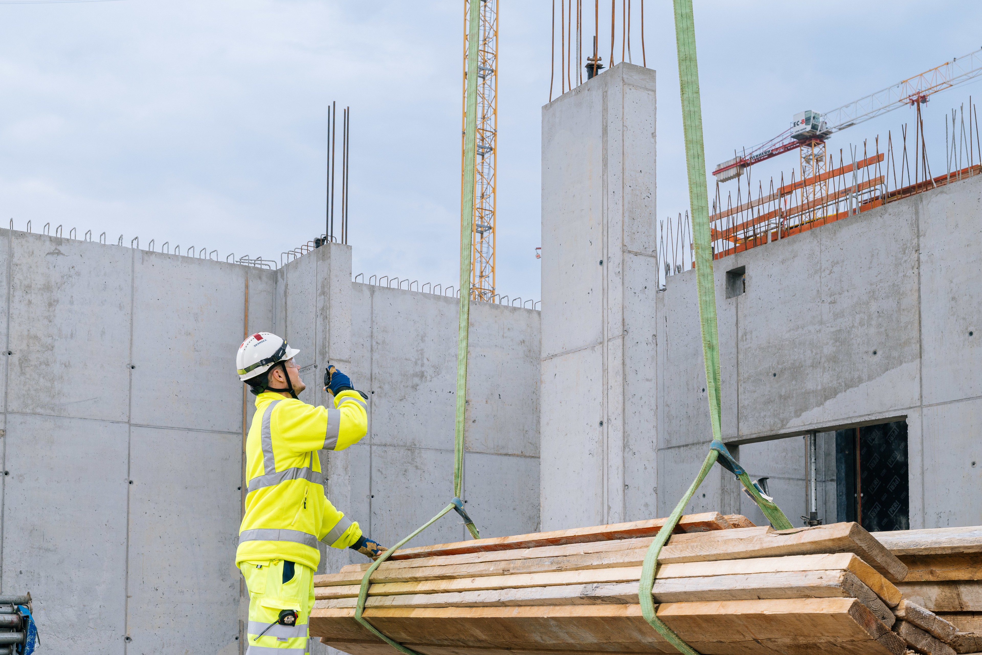 Construction workers lift wood at the construction site A construction worker in high-visibility equipment operates a crane lifting wooden planks at a construction site.
