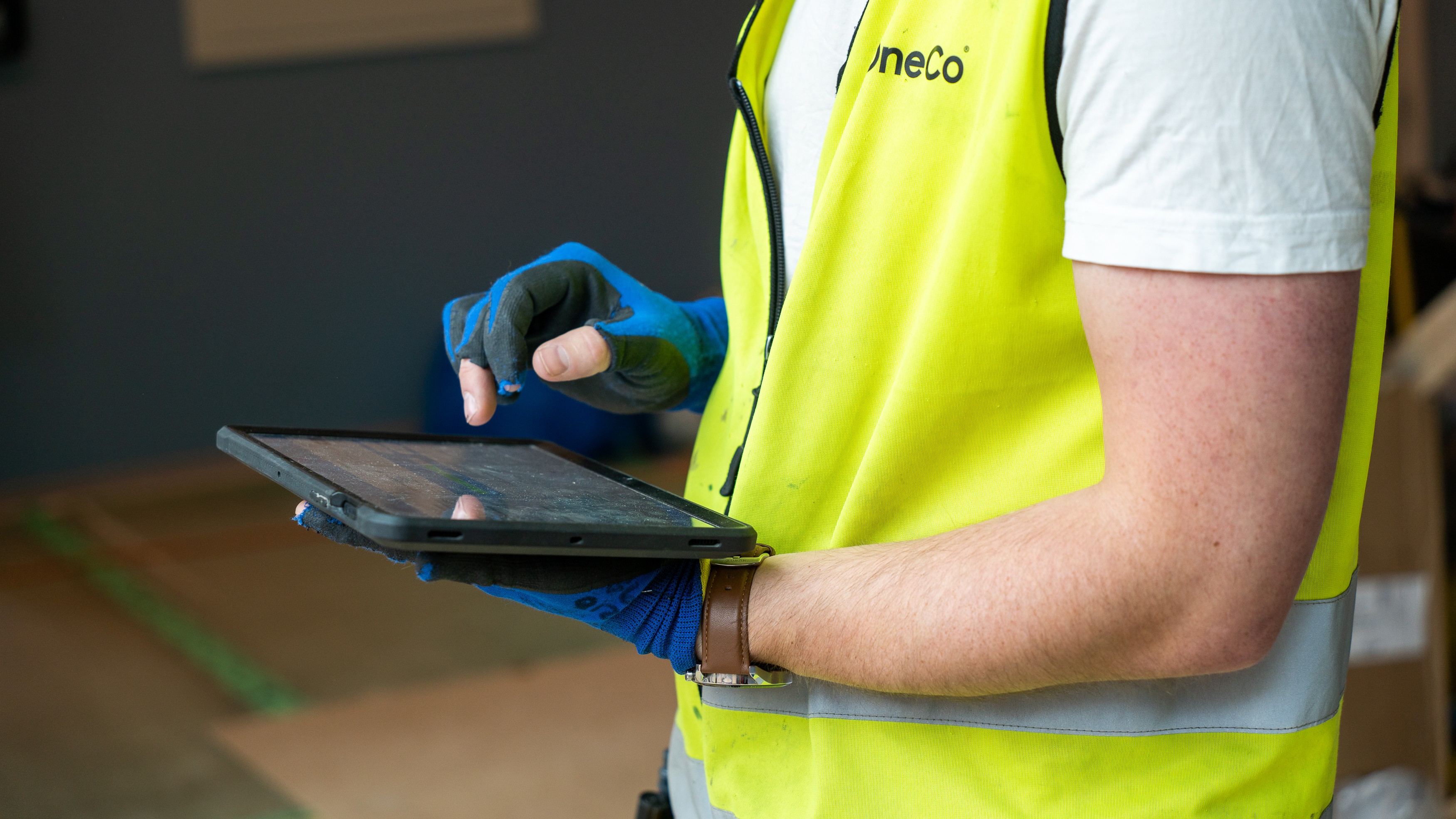 Construction workers use tablet for site management A worker in a yellow vest and gloves is using a tablet in a construction environment.