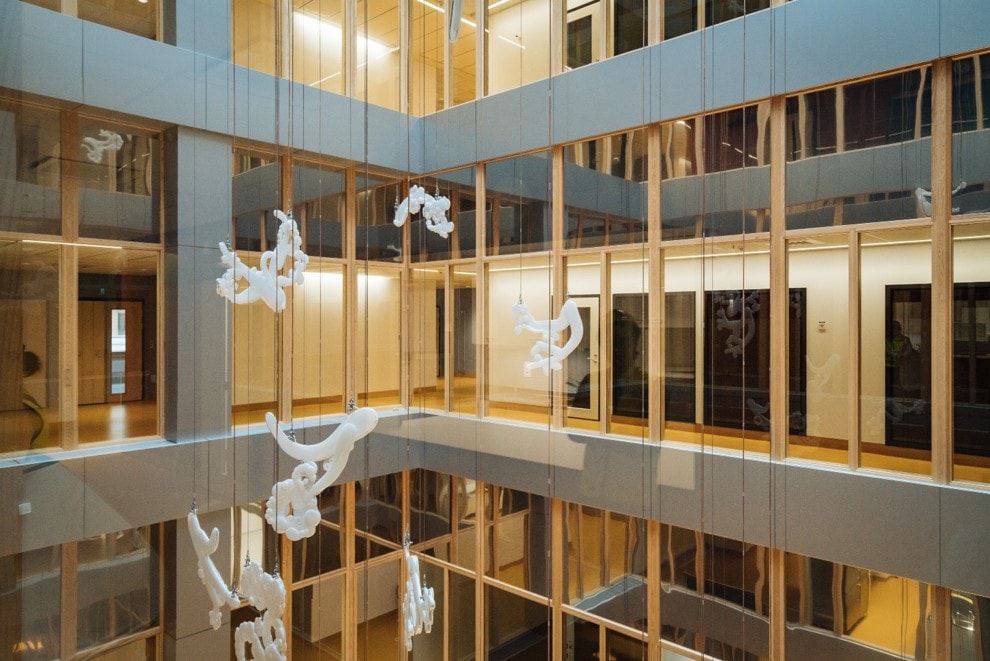 Modern atrium with hanging white sculptures surrounded by glass walls and wood accents.