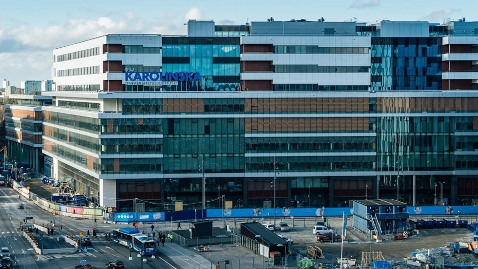 Modern byggnad med glasfasad märkt "Karolinska," omgiven av urban infrastruktur och trafik.