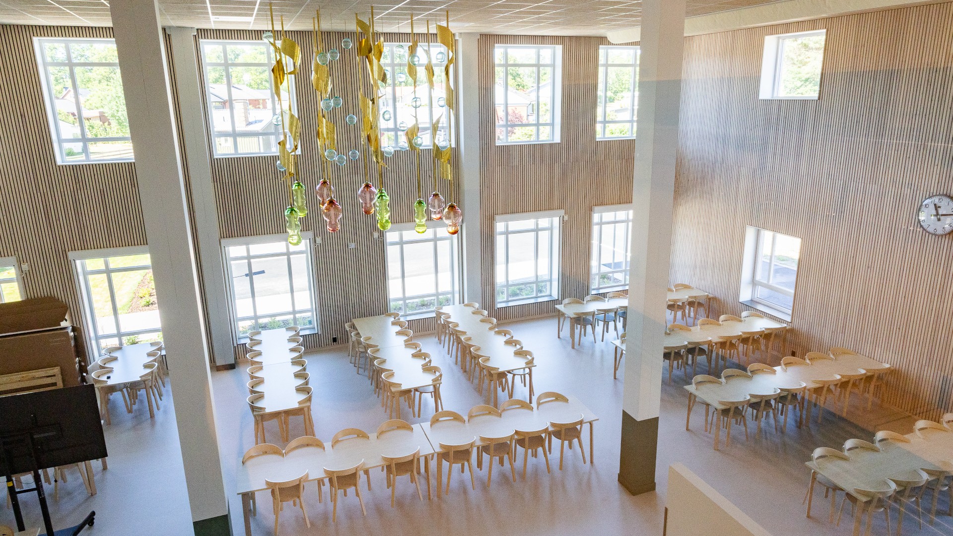 Genom partnering har Nybro kommun och Skanska byggt Västerängsskolan. Rymlig matsal med stora fönster, träbord, stolar och färgglada hängande lampor.