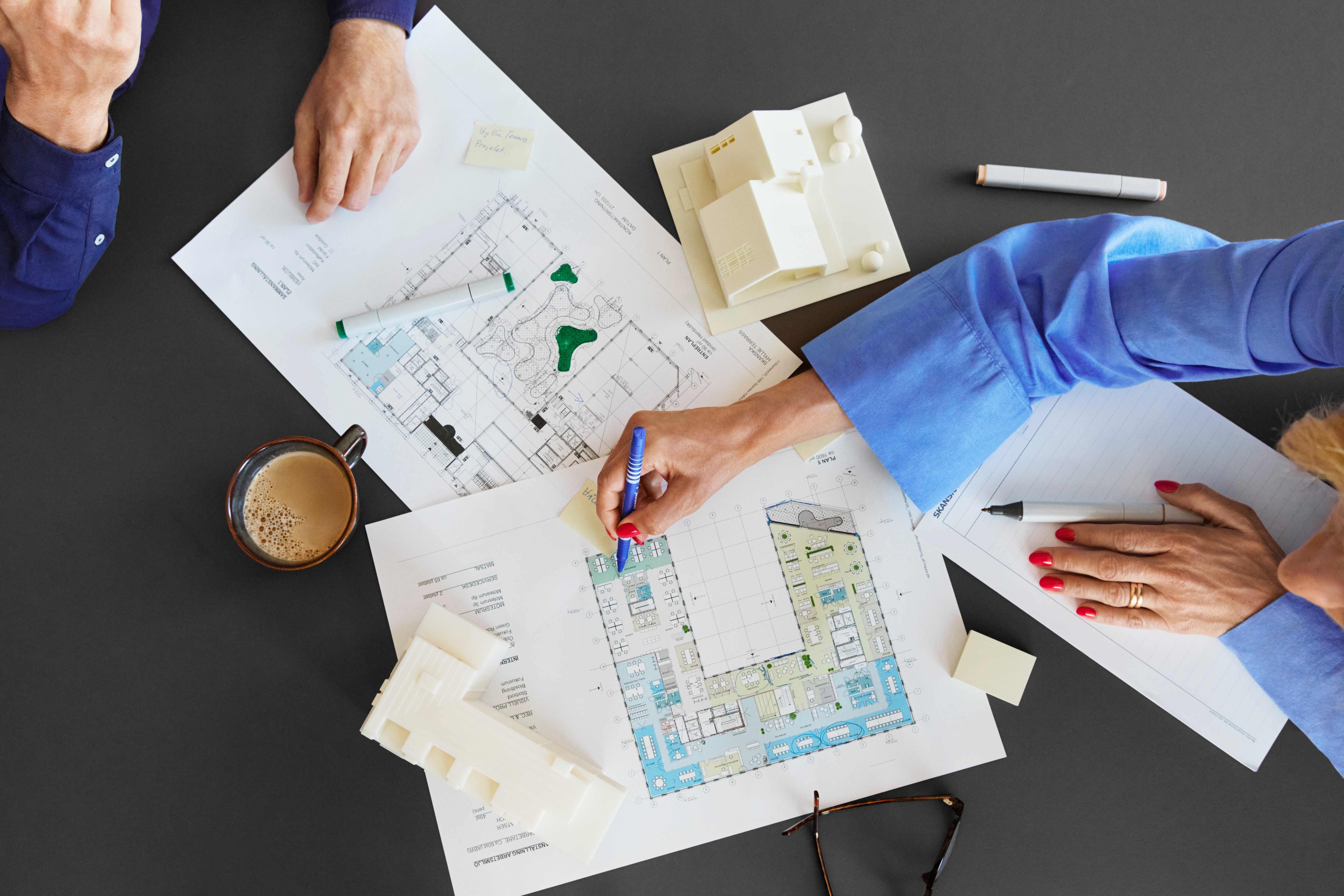 Architects examine building drawings and models on a table with coffee and markers.