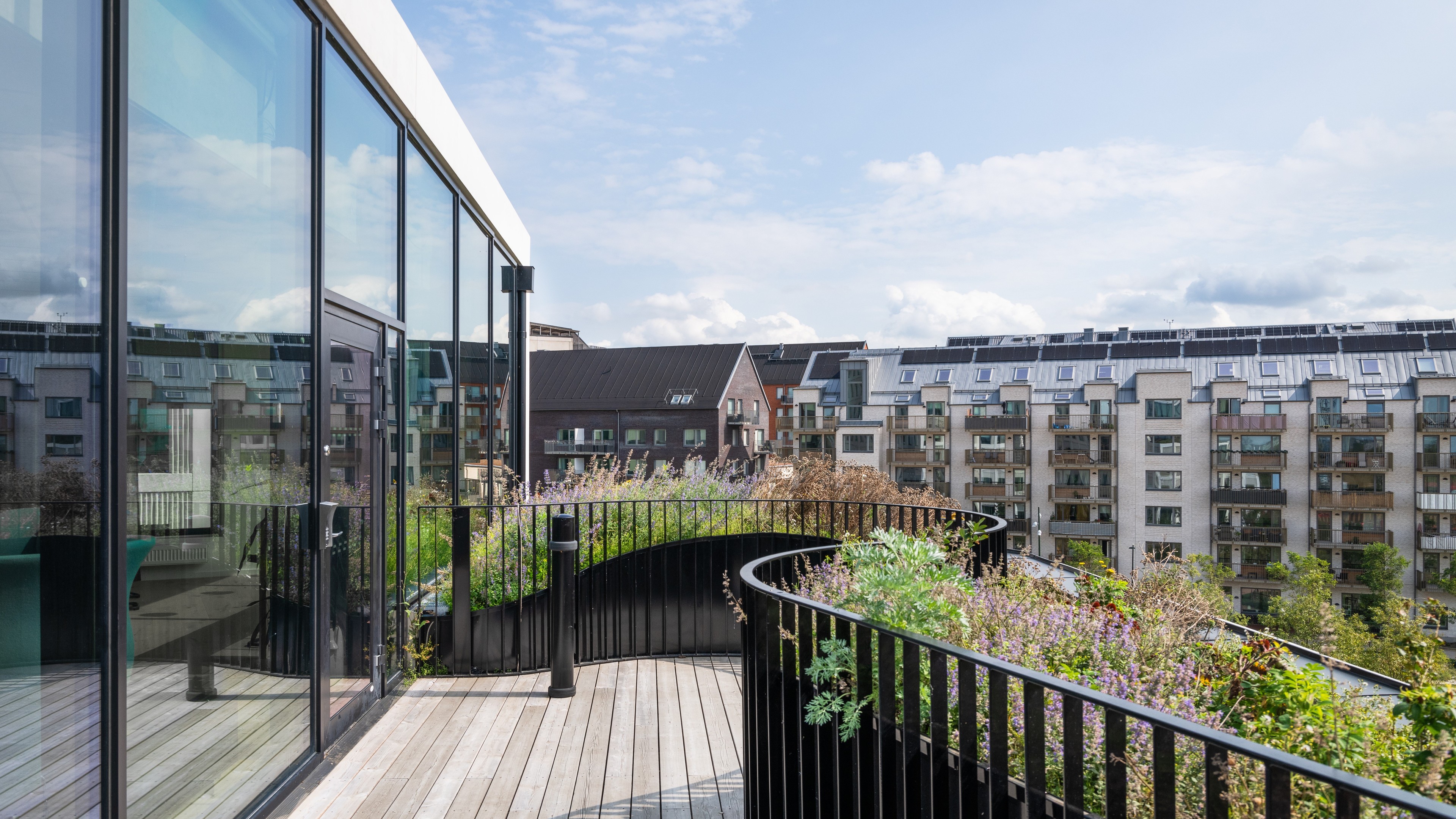 Modern takterrass med glasväggar, trädäck och utsikt över stadsträdgård.