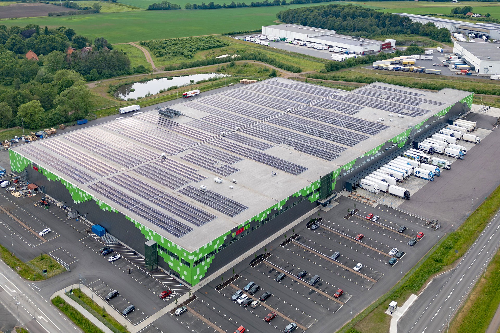 Flygvy av industriellt lager och omgivande landskap Flygvy över en logistikknutpunkt omgiven av grönska, som visar lagerbyggnader och transportvägar.