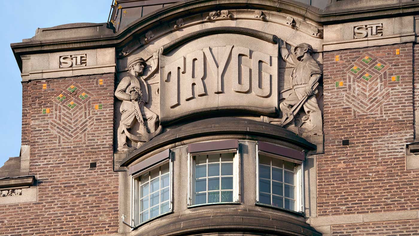 Historisk tegelbyggnadsfasad med stenskulpturer och ordet "TRYGG" framträdande visat.