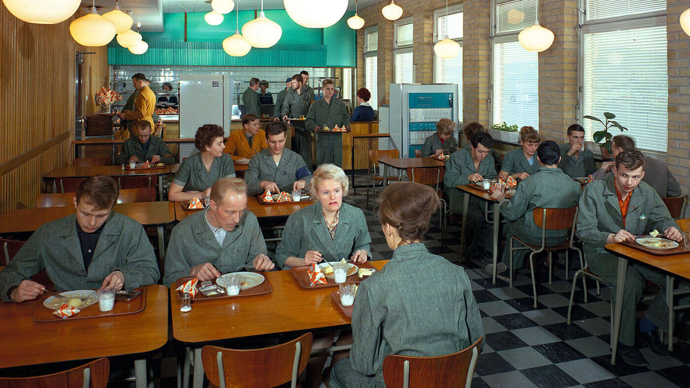 A group of people in uniform enjoying a meal in a retro-style cafeteria setting.