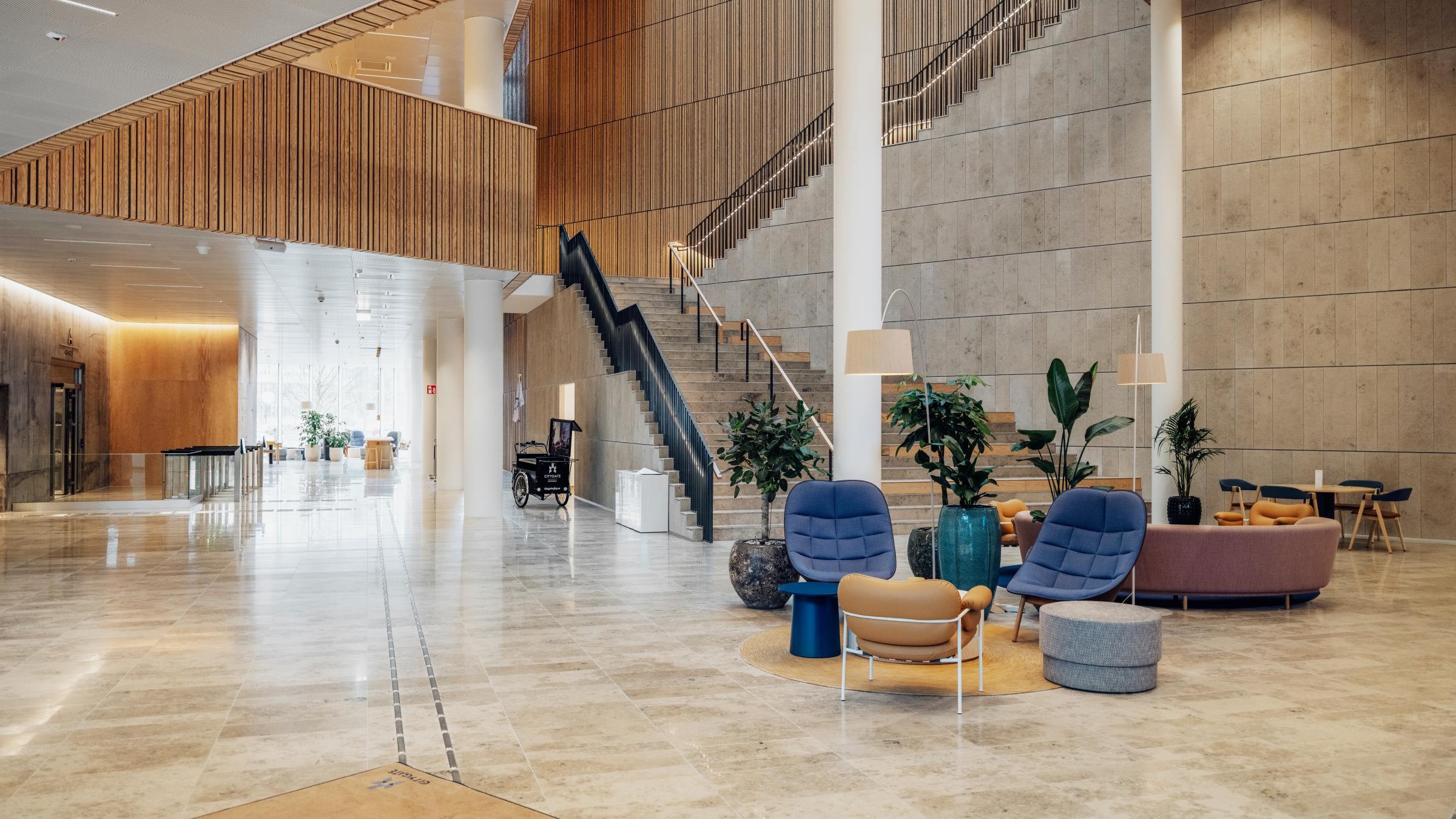 Modern kontorslobby med stilfulla sittplatser och trappa Modern hotellobby med elegant sittgrupp, växter och trappa, badad i naturligt ljus.