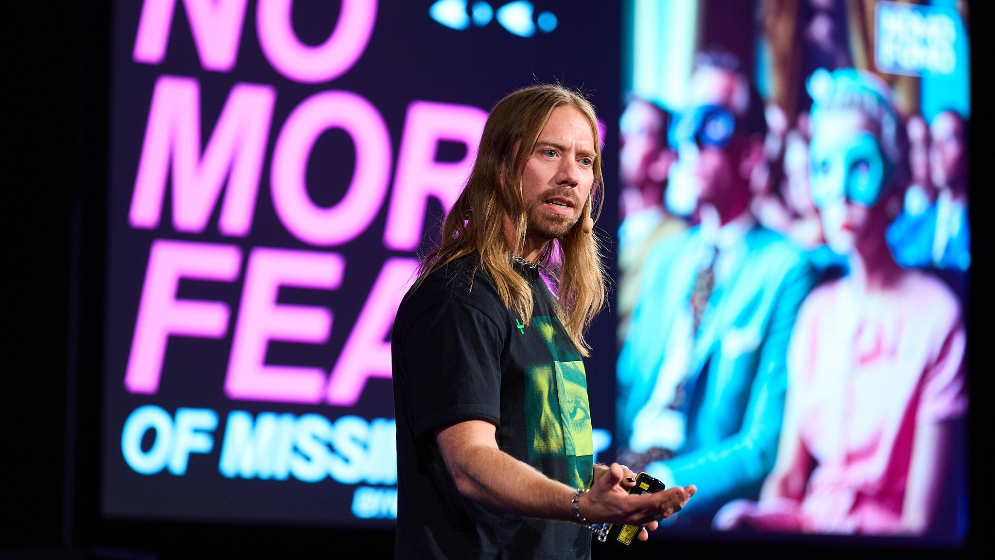 Talare som presenterar på scen med ett livfullt "No More Fear"-budskap i bakgrunden.