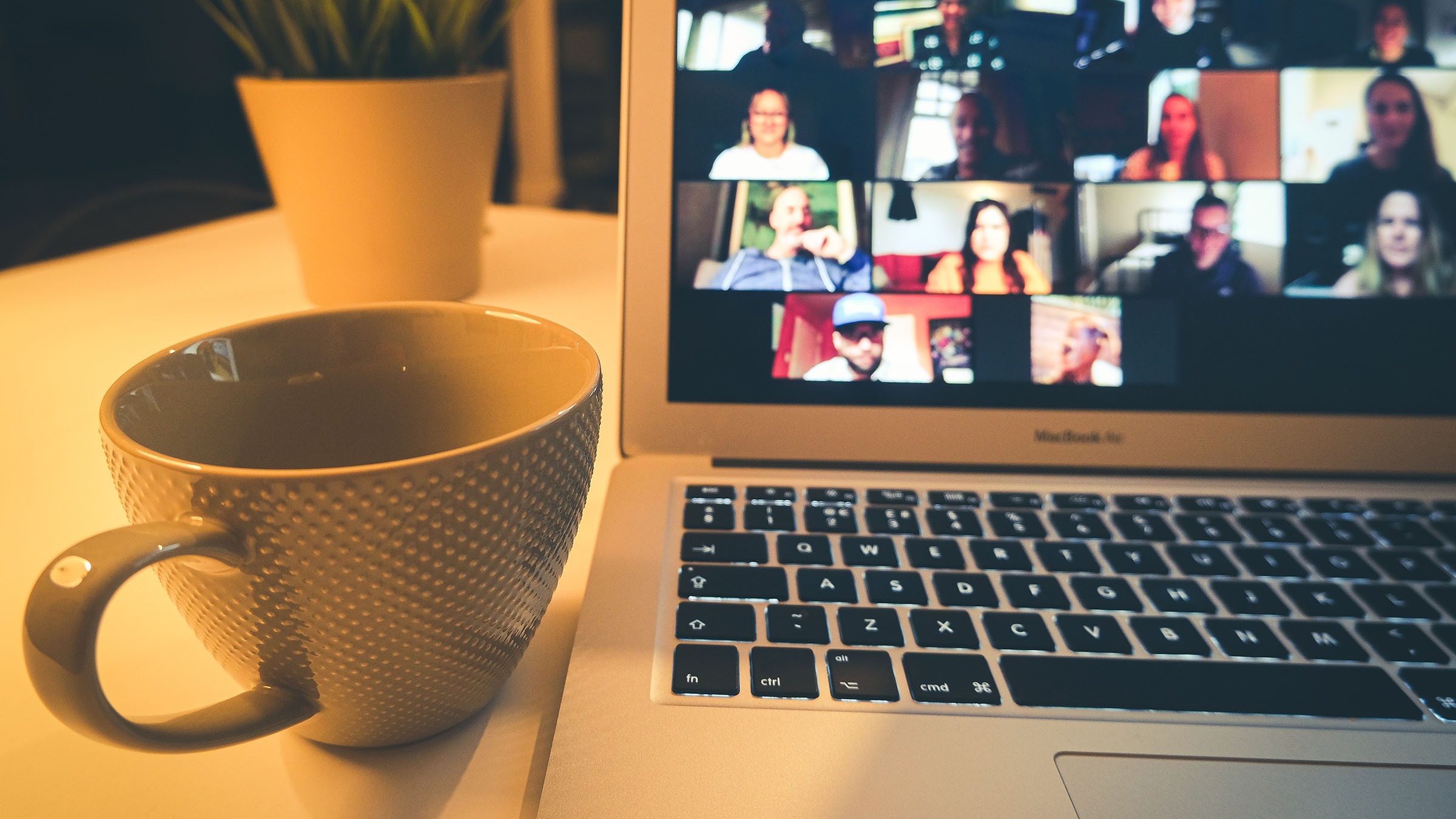 Bättre digitala möten Laptop som visar ett virtuellt möte bredvid en strukturerad mugg, vilket belyser dynamiken i distansarbete.