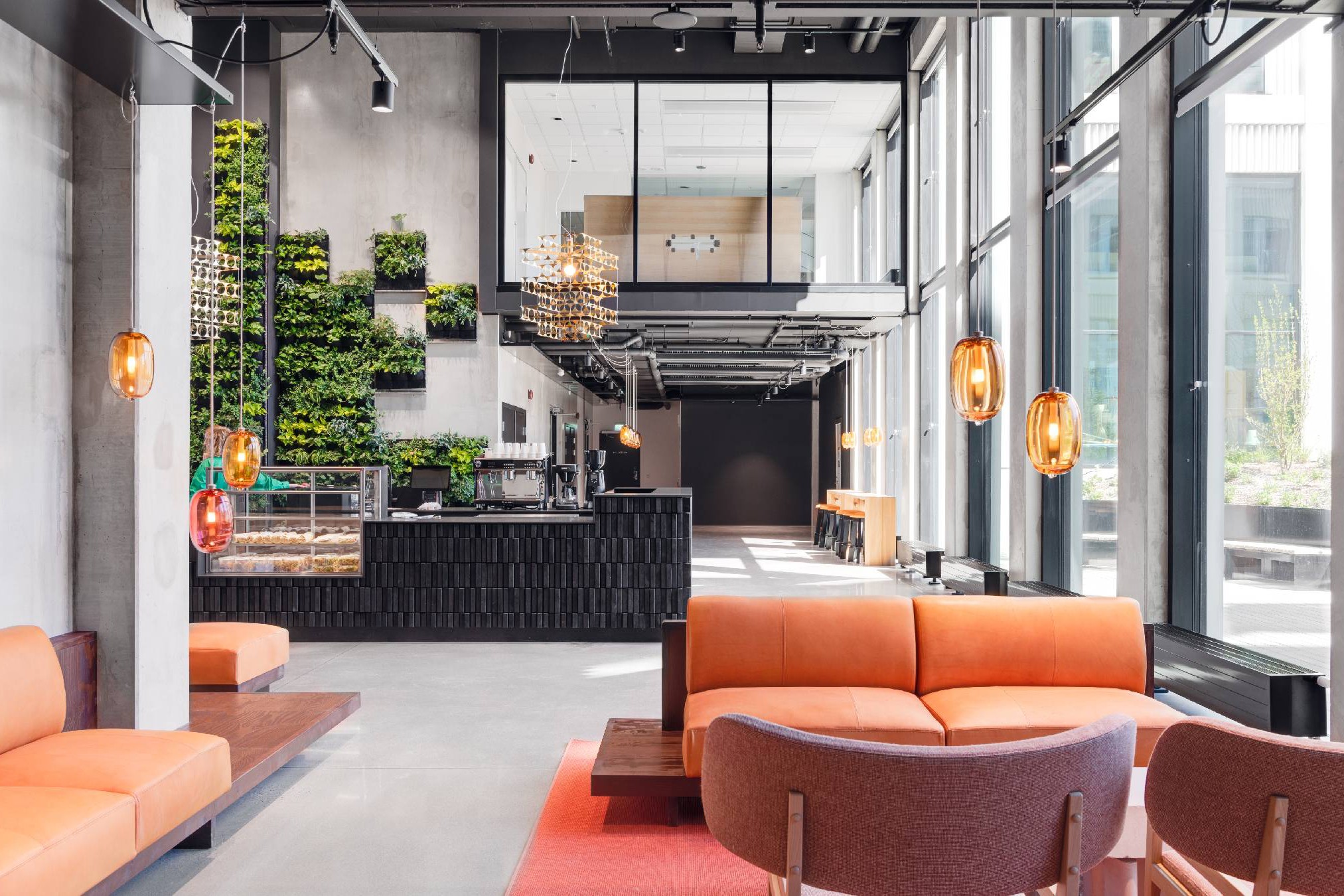 Modern kontorslounge med livfull design och grönska Modern lobby med orange sittplatser, en grön vägg och hängande lampor i en rymlig, ljus miljö.