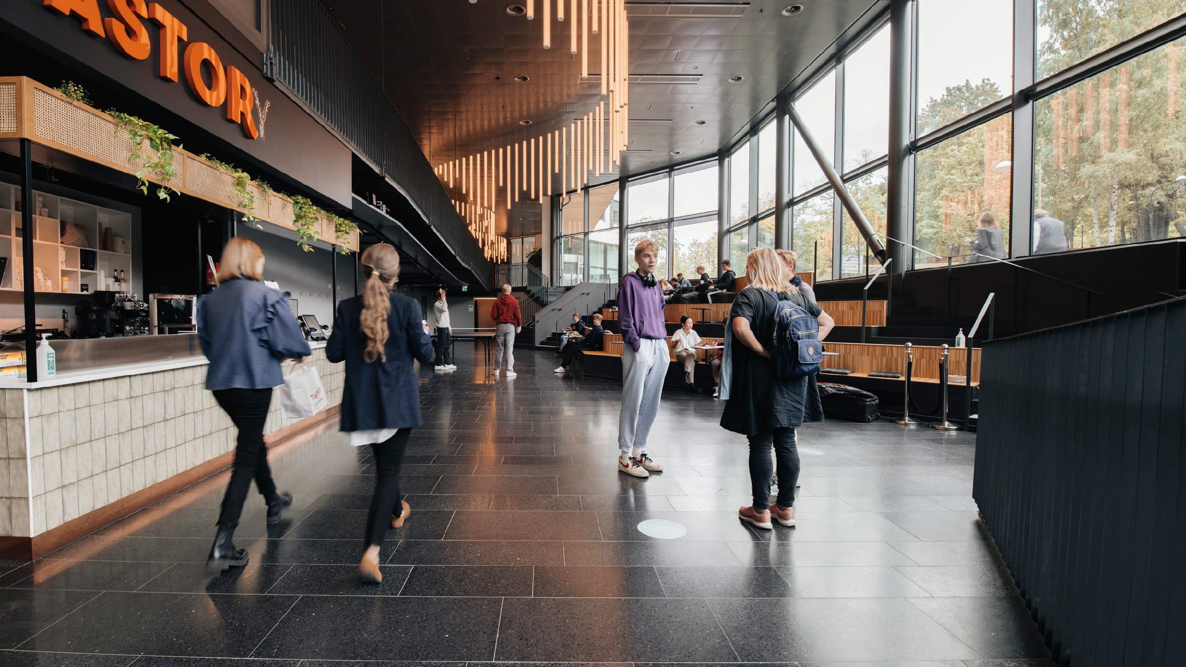 Modern lobby med människor som umgås och stilren design Modern lobby med människor som umgås, med stora fönster och stilfulla hängande lampor.