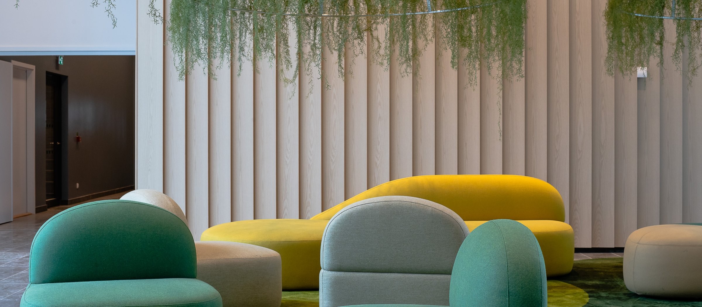 Kontorstrend: Från öppet landskap till syftesdrivet Modern loungeområde med livfulla gröna och gula sittplatser, vertikala träpaneler och hängande växter.