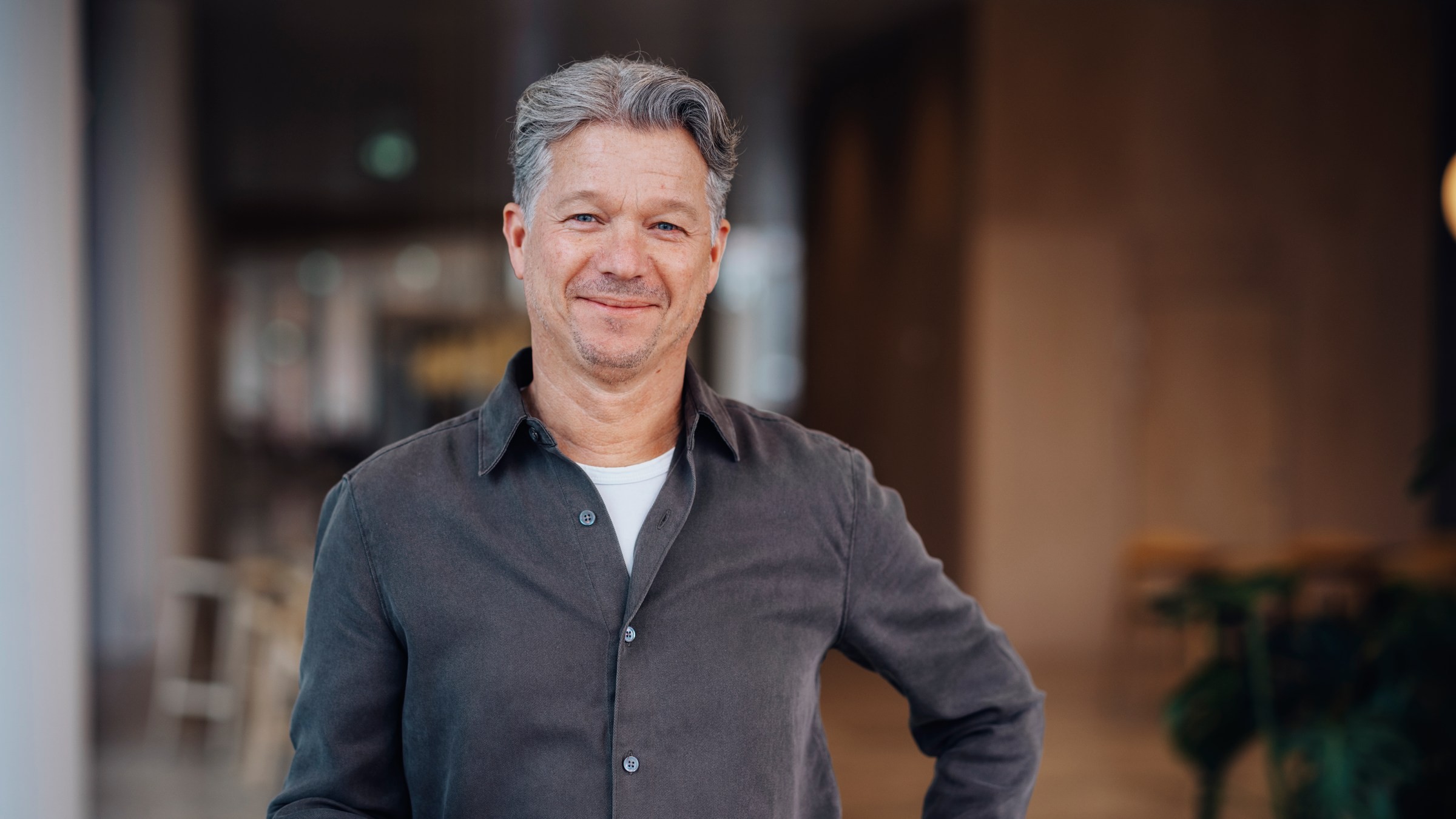 Stilig man i modern interiör bär avslappnad klädsel En man med grått hår, klädd i en grå skjorta med knappar, står i ett modernt inomhusutrymme.