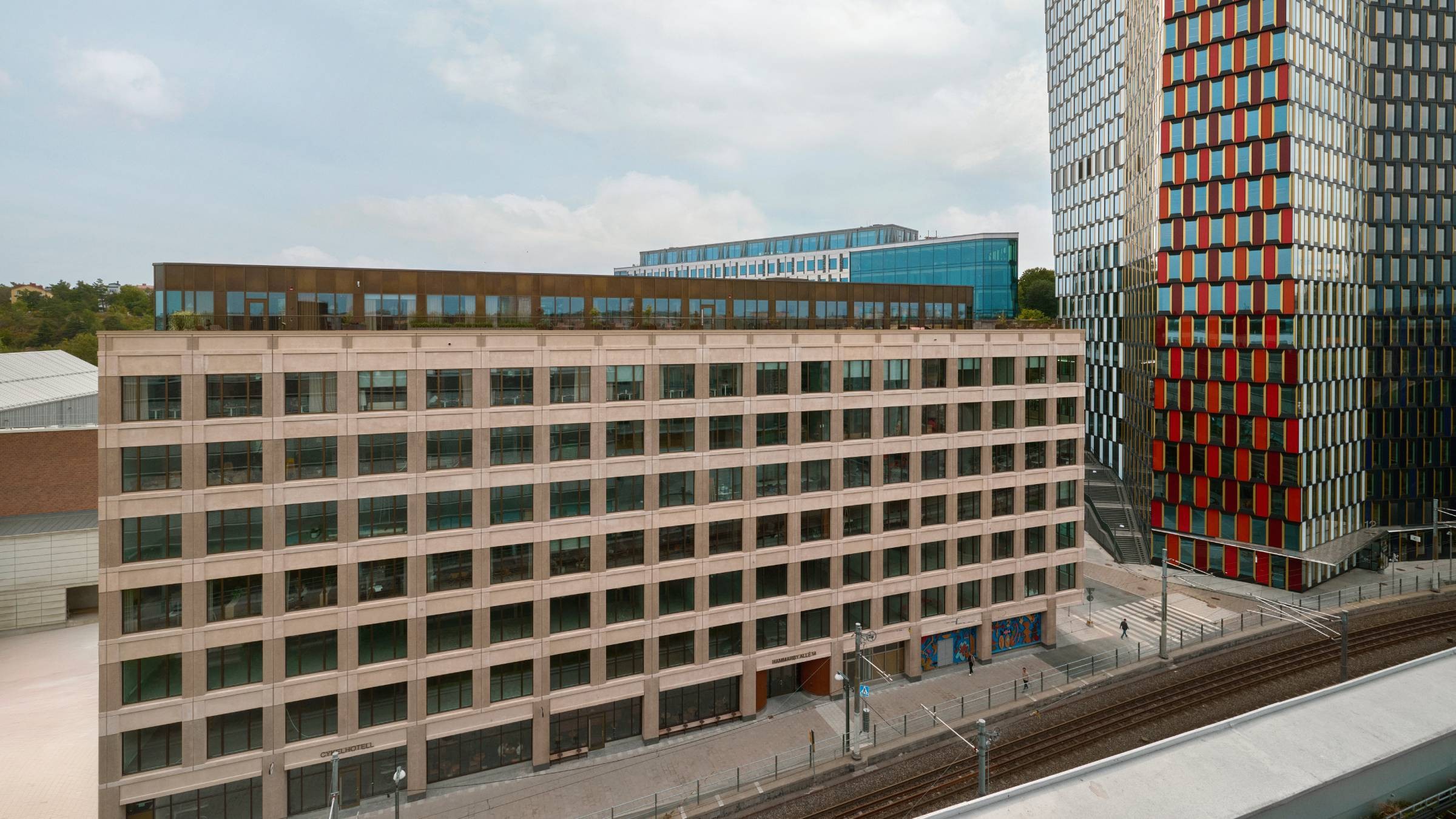 Modern urban arkitektur med livfulla byggnadsfasader Modern stadslandskap med en beige kontorsbyggnad och en färgglad höghus nära järnvägsspår.