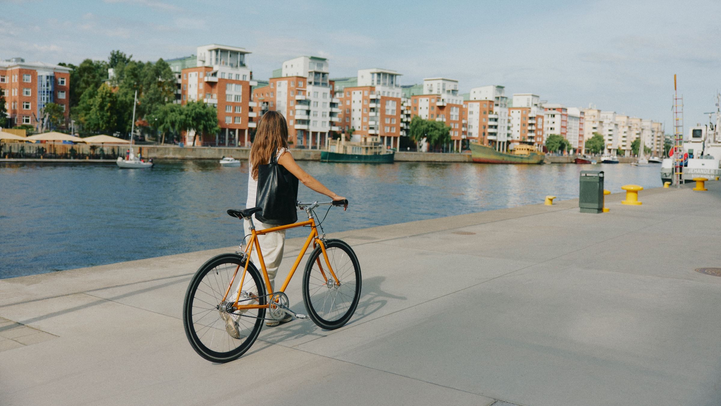 Cyklist njuter av utsikt över floden i stadsområde Kvinna cyklar längs en flodpromenad med moderna lägenheter i bakgrunden.