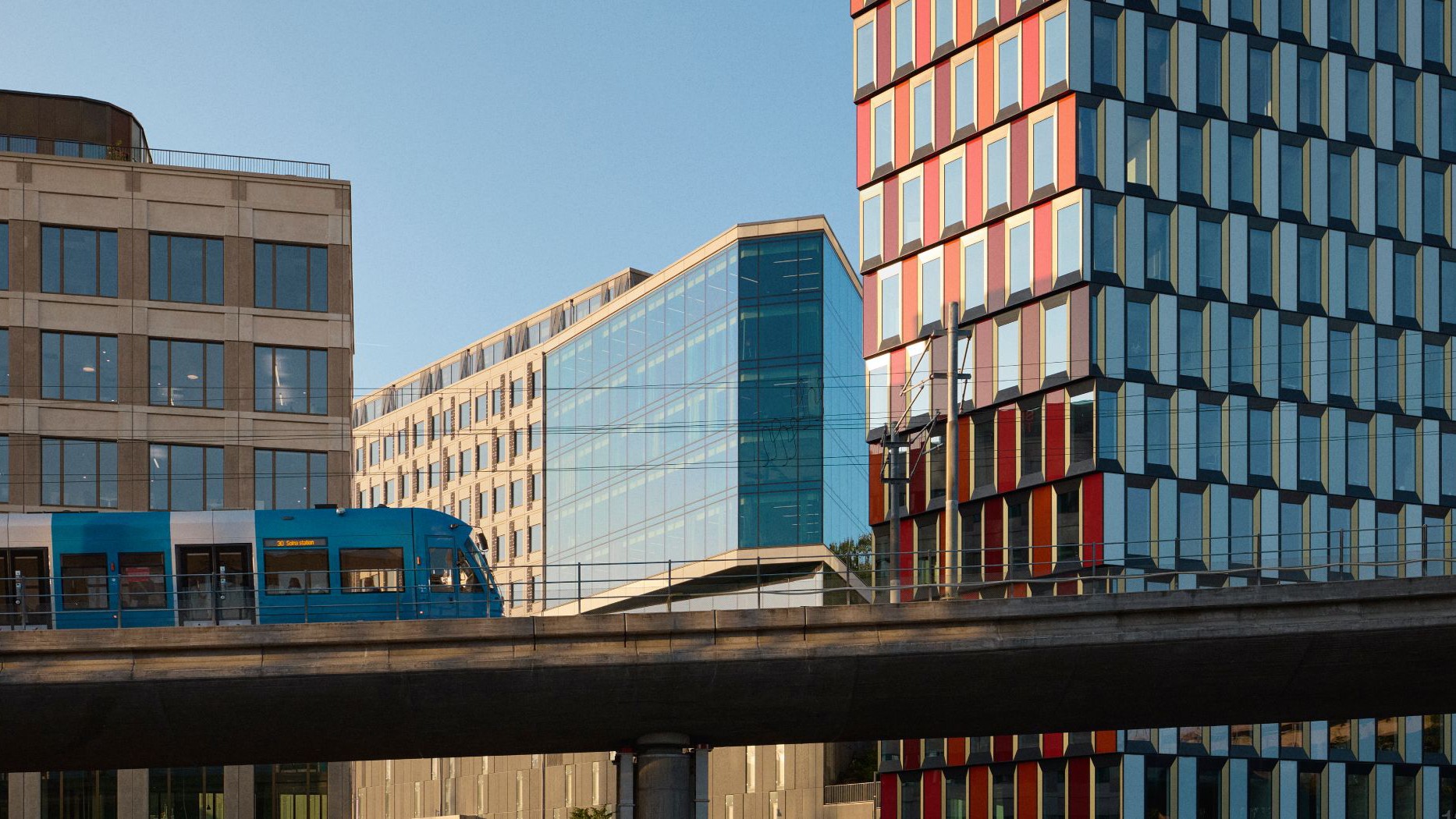 Modern urban arkitektur med tåg i stadsbild Modern spårvagn korsar en bro nära moderna glasbyggnader i en urban miljö.