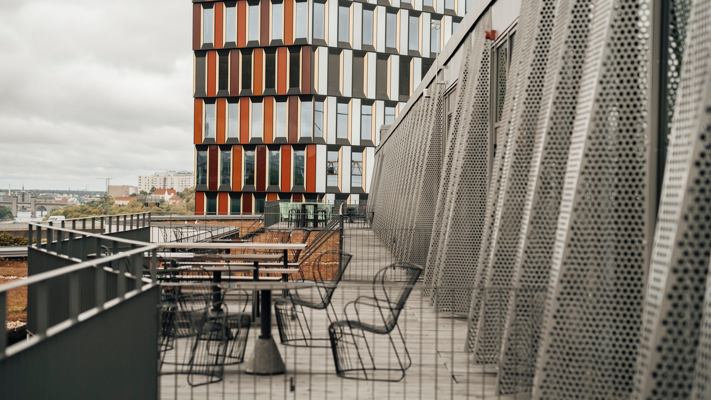 Modern utomhusterrass med metallmöbler, med utsikt över en unik byggnad med färgglada paneler.