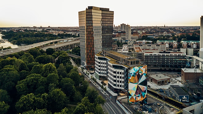 Flygvy över en stadsbild med en färgglad geometrisk muralmålning på en modern byggnadsfasad.