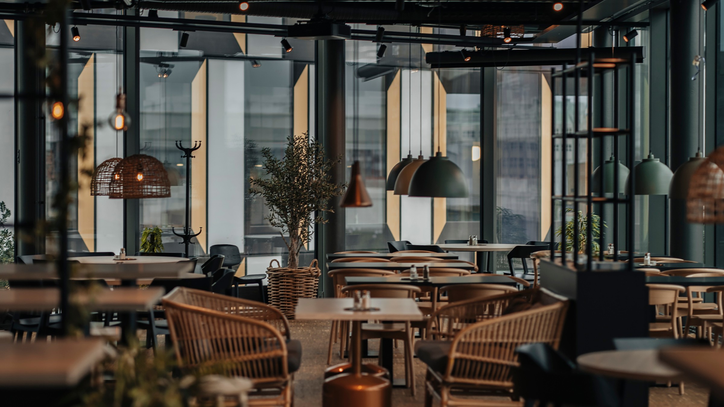 Modern restauranginteriör med korgstolar, hängande lampor och stora fönster.