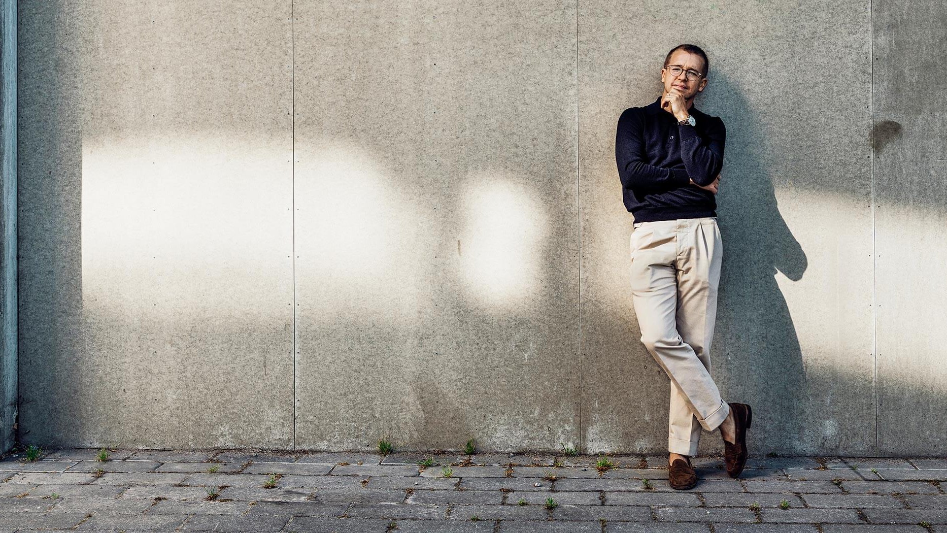 Beteendepsykolog Niklas Laninge A person in dark shirt and light pants leans casually against a sunlit concrete wall outside.