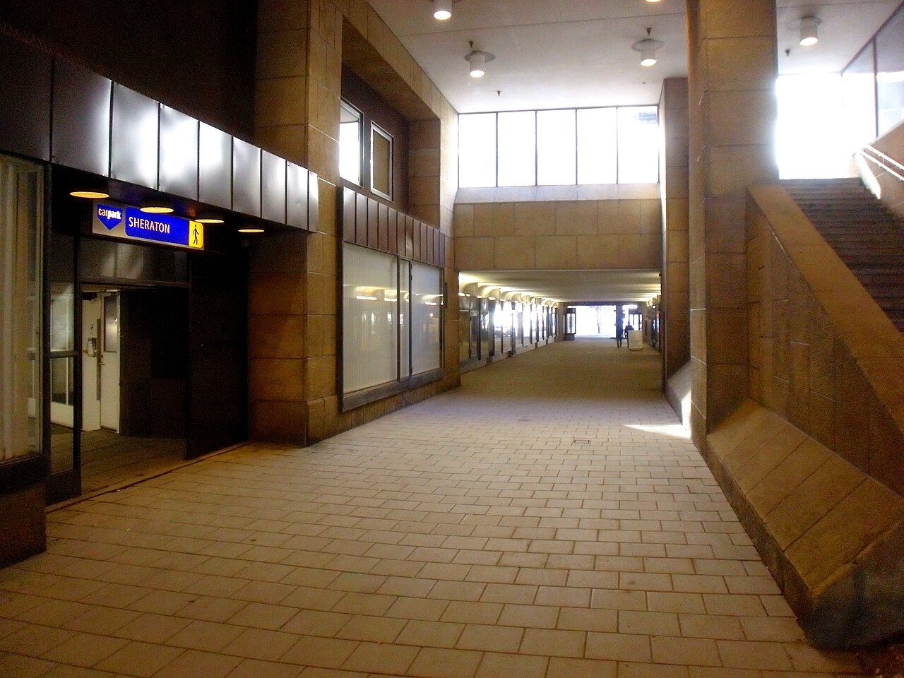Inomhuskorridor med kaklat golv, stenväggar och en upplyst Sheraton-hotellingångsskylt.