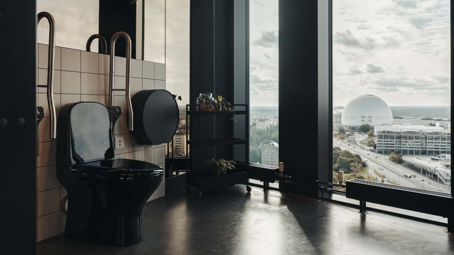 Modern svart toalett med stora fönster med utsikt över en stadssilhuett och unik arkitektur.