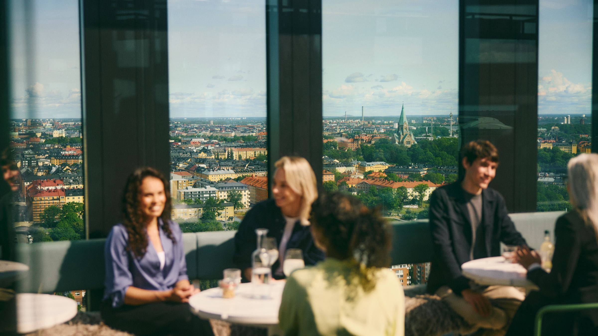 Personer som har ett möte i ett modernt kontor med utsikt över stadssilhuett genom stora fönster.