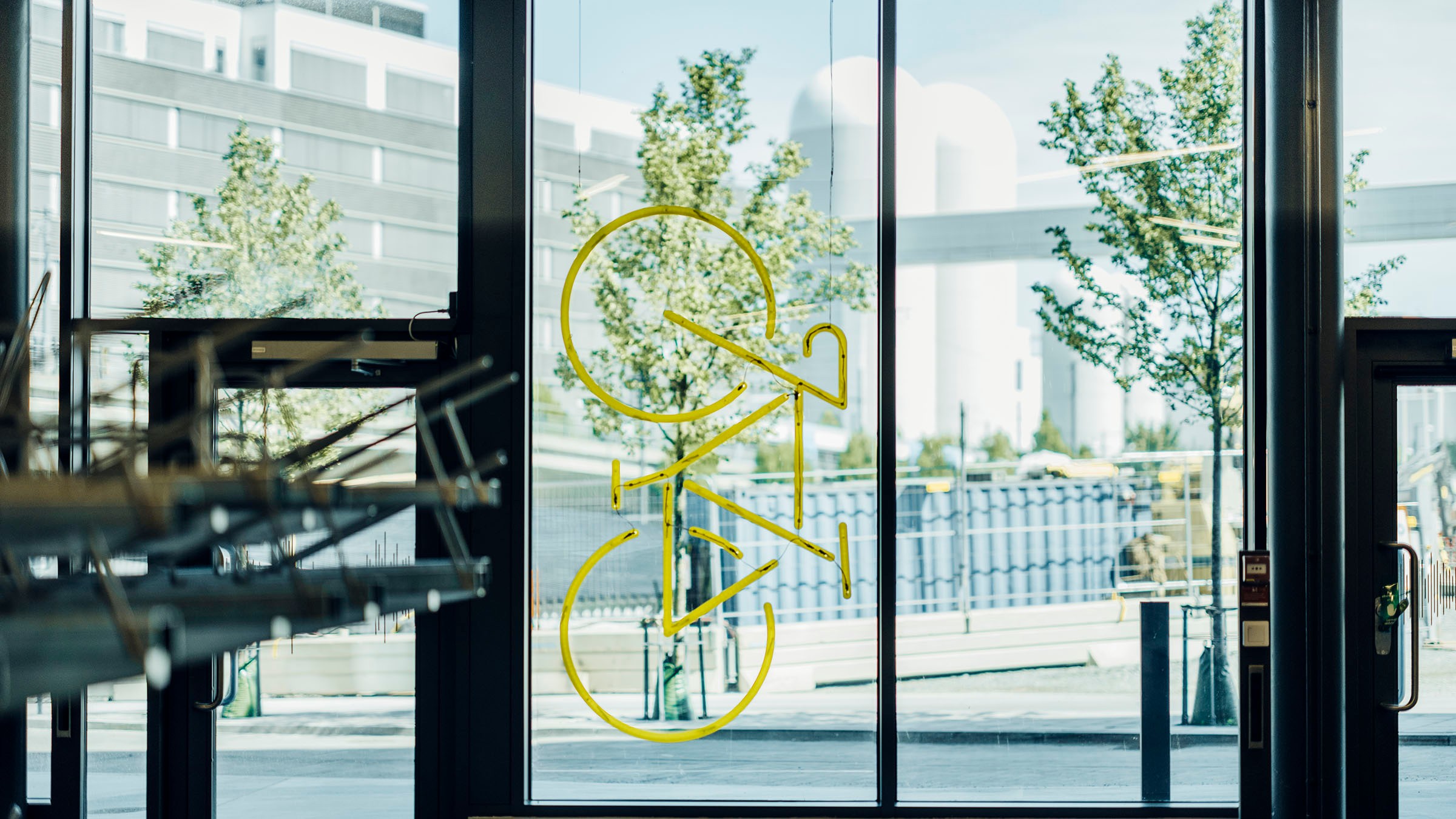 Modern kontorsentré med gul logotyp och glasdörrar Gul cykelgrafik på glasdörr med stadslandskap och träd i bakgrunden.