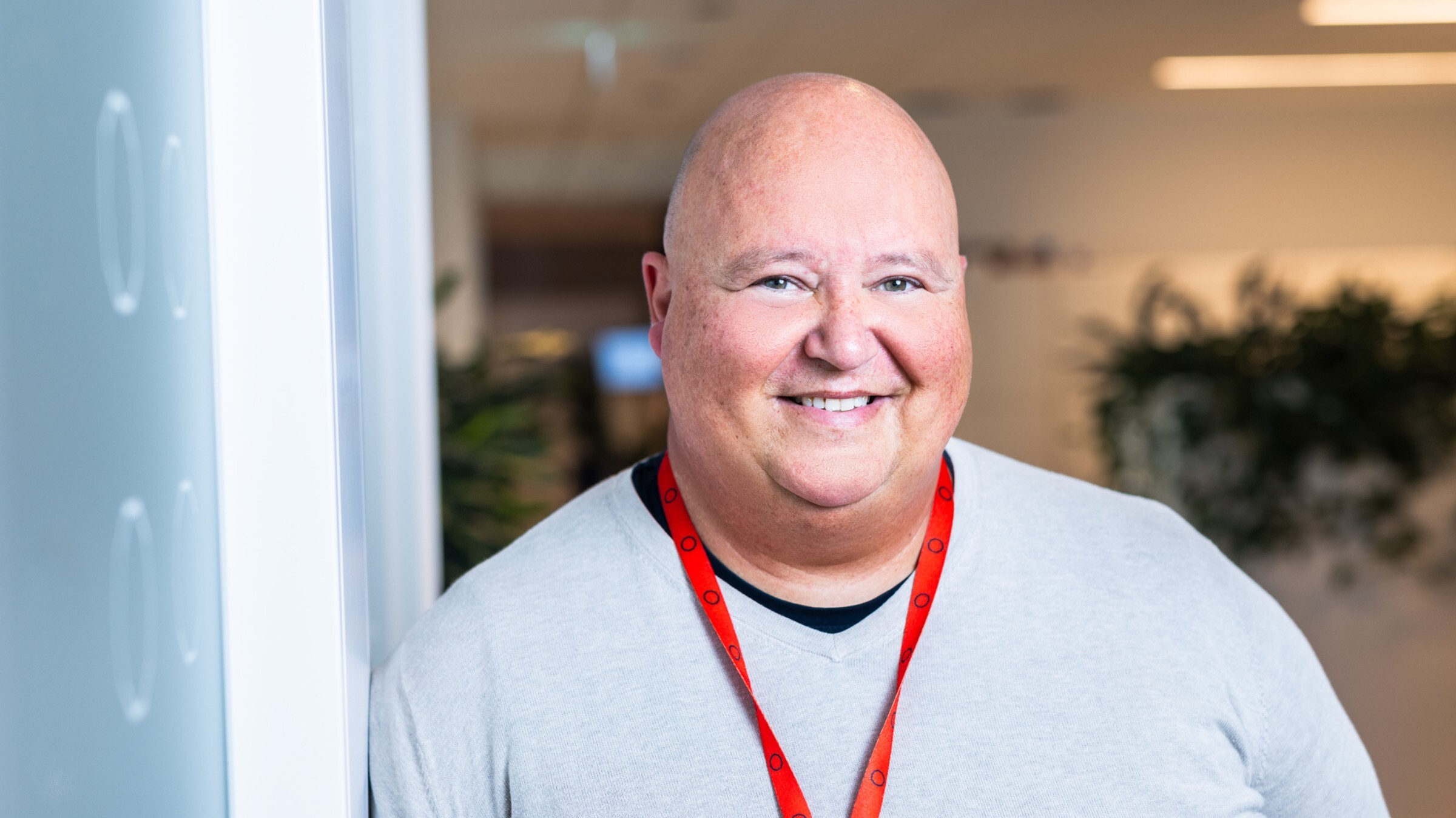 Medelålders man som bär en vit tröja och ett rött nyckelband stående inomhus vid en vägg.