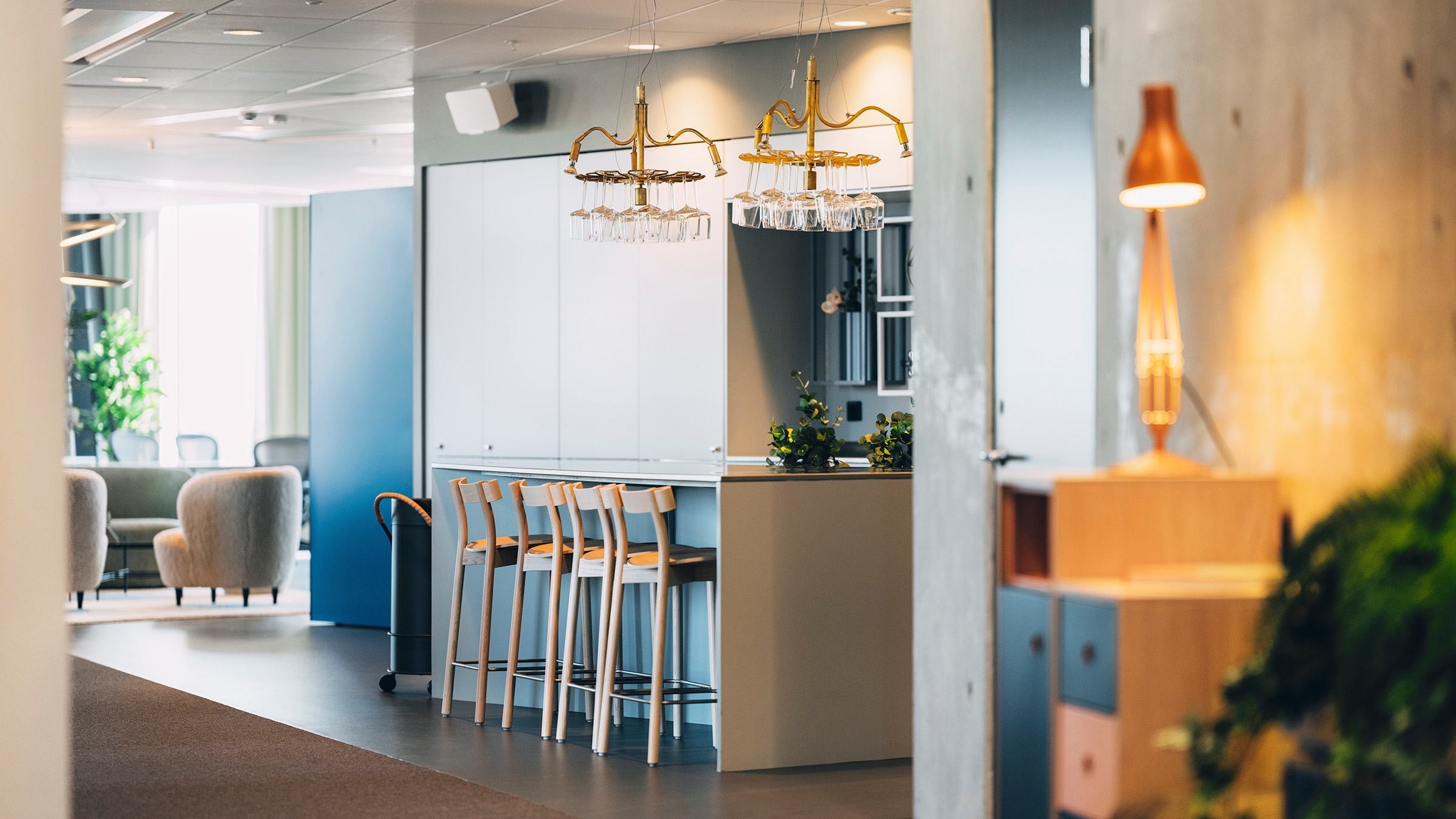Modern kontorslounge med stilfulla sittplatser och belysning Modern kontorskök med barstolar, elegant belysning och mysiga sittplatser i bakgrunden.