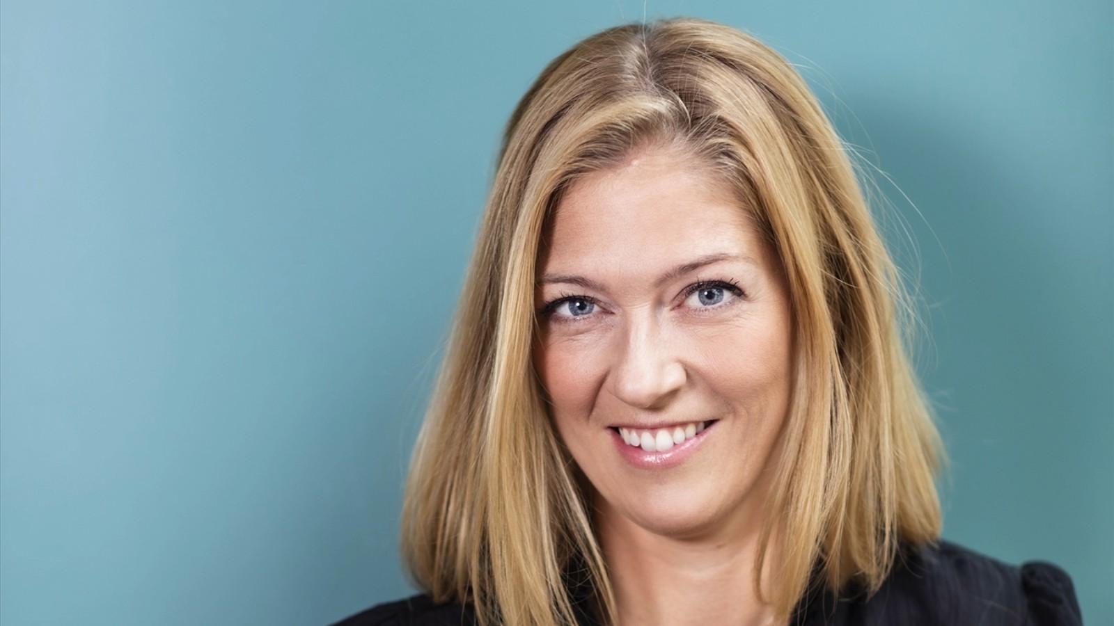 Blonde Woman with Shoulder-Length Hair Against Blue Background Blond kvinna med rakt hår som bär en svart topp mot en blå bakgrund.