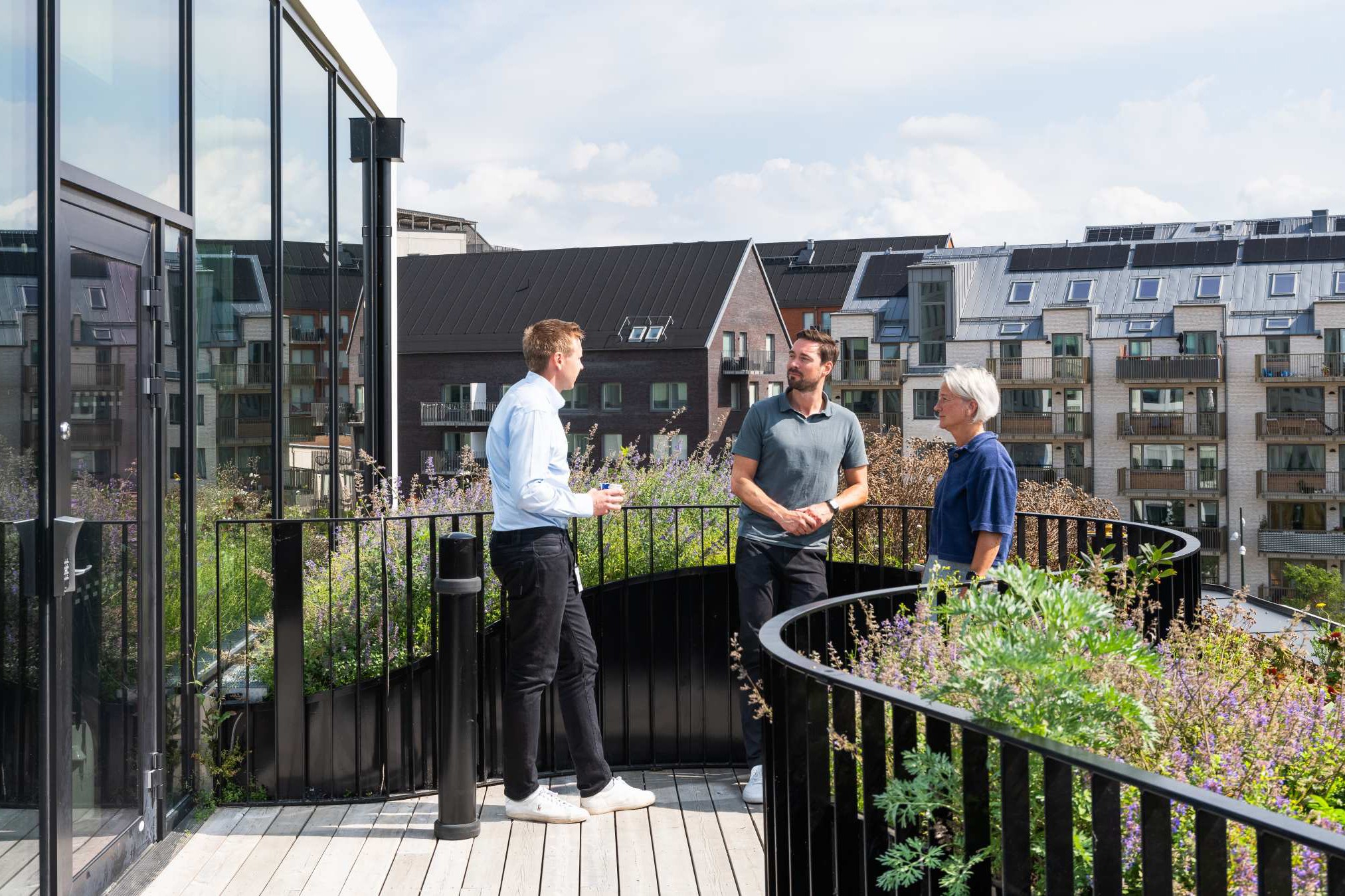 Modern takmöte med natursköna stadsutsikter Tre män samtalar på en modern takterrass med utsikt över stadssilhuetten och frodig grönska.