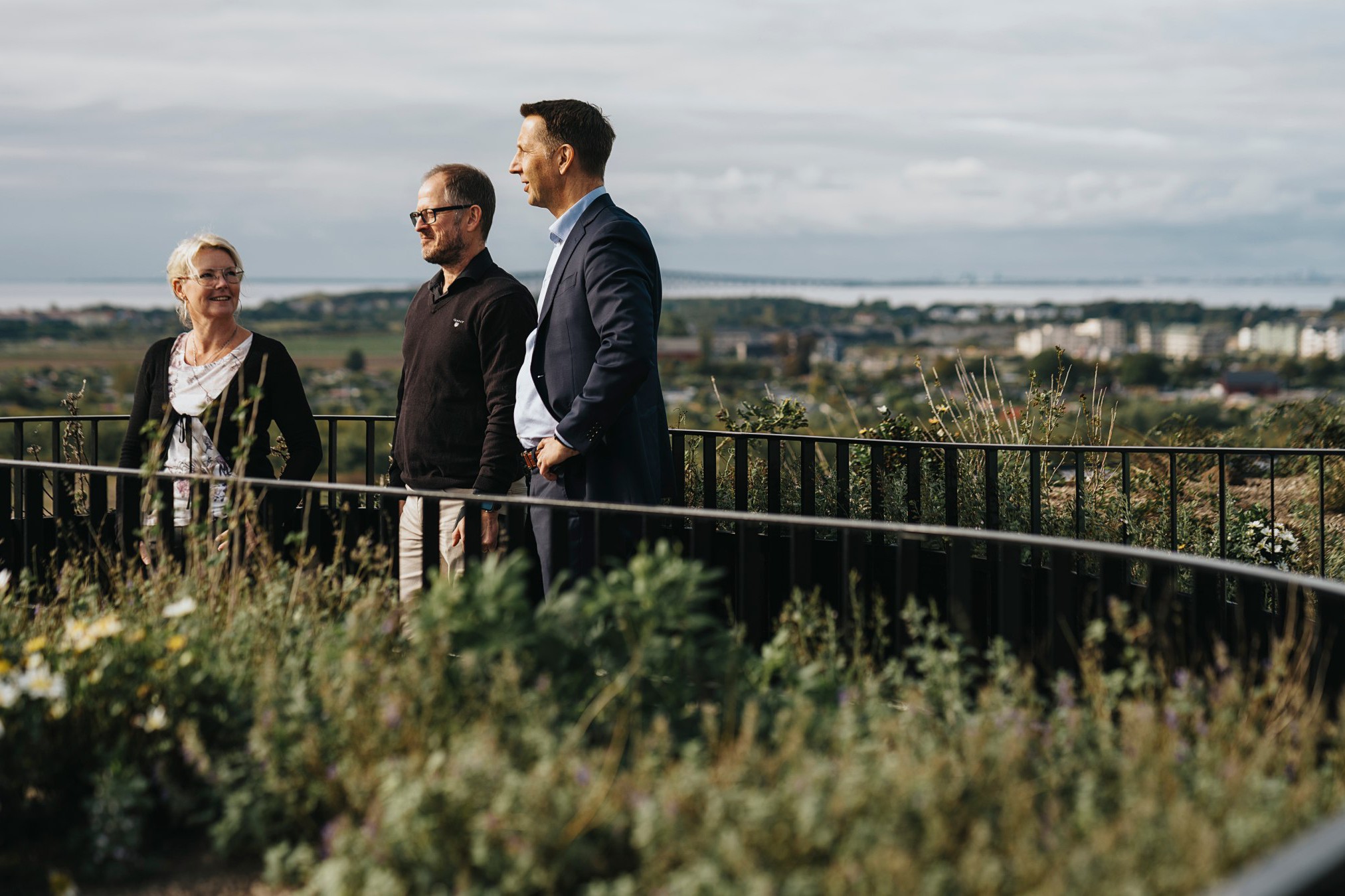 Affärsproffs njuter av den natursköna urbana landskapsvyn Tre personer står på en naturskön utsiktspunkt med urbana och naturliga vyer i bakgrunden.